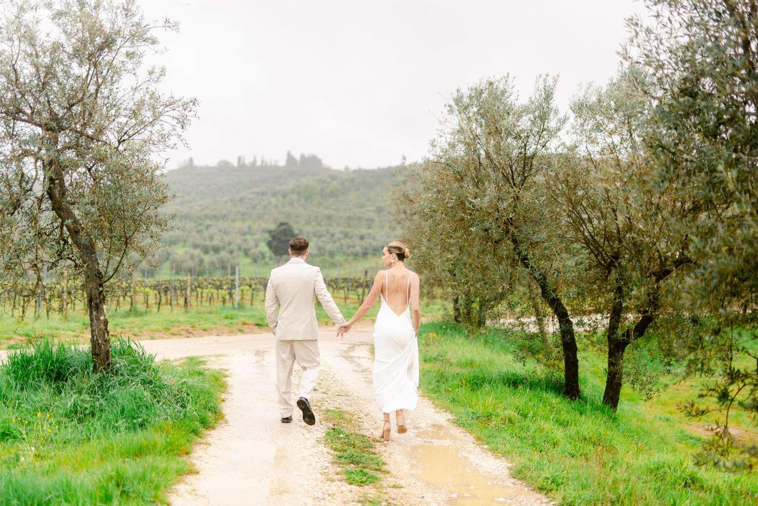 Couple strolls through scenic olive grove on their wedding day.