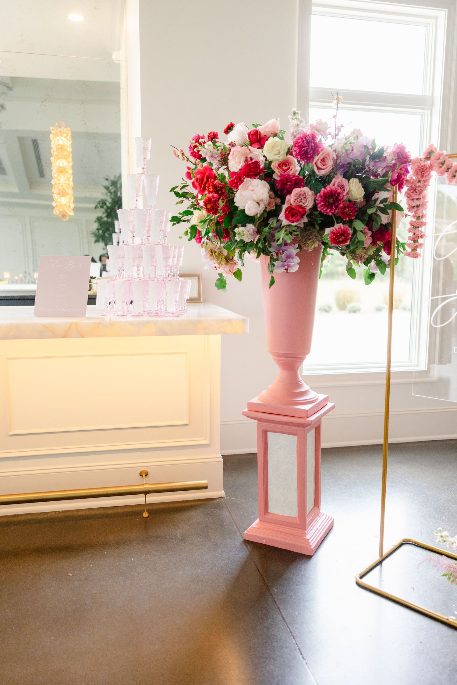 Pink pedestal vase with luxurious floral arrangement against white piano backdrop.