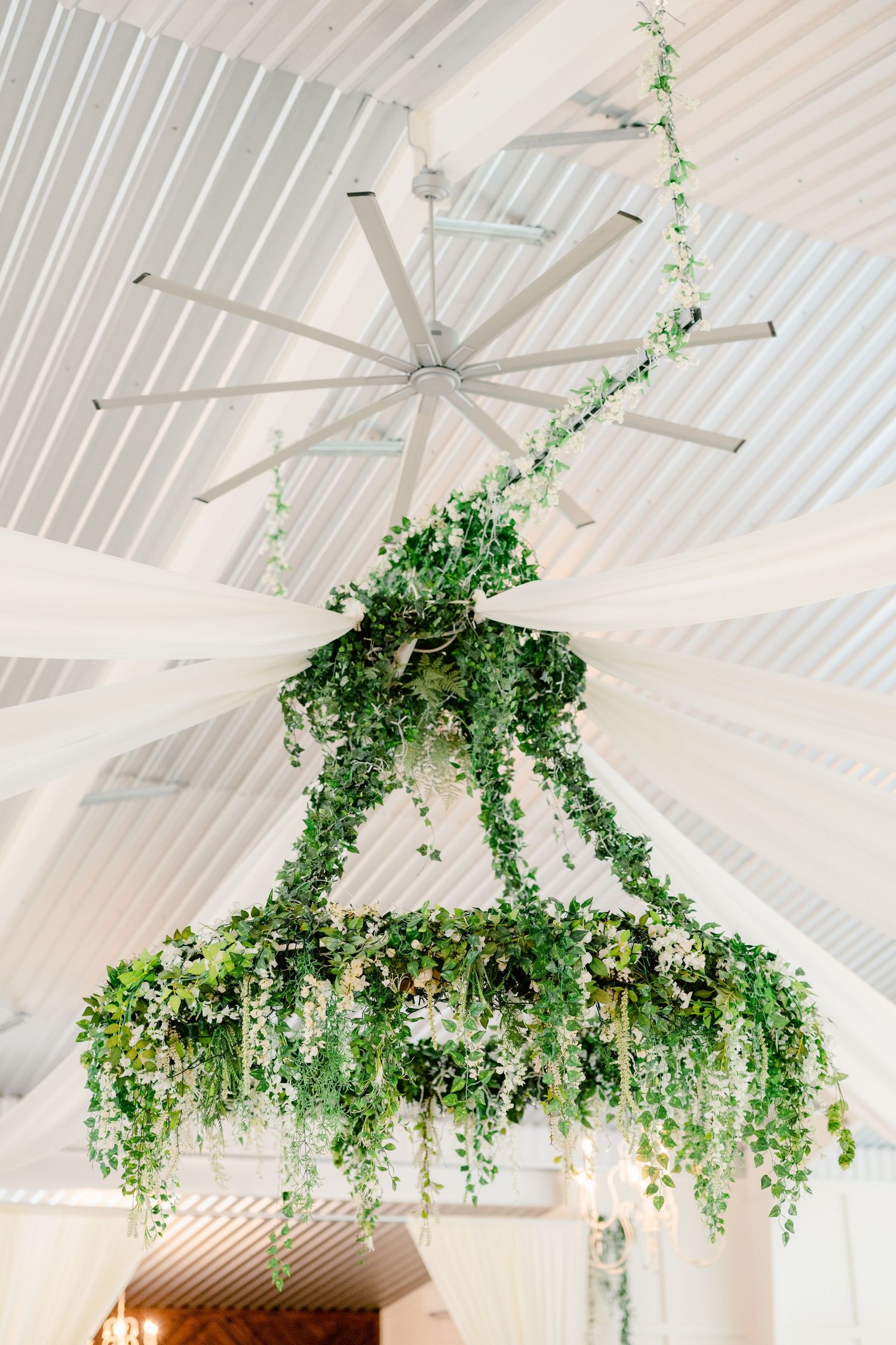 White vaulted ceiling with hanging greenery installations and chandelier creating an ethereal garden atmosphere.