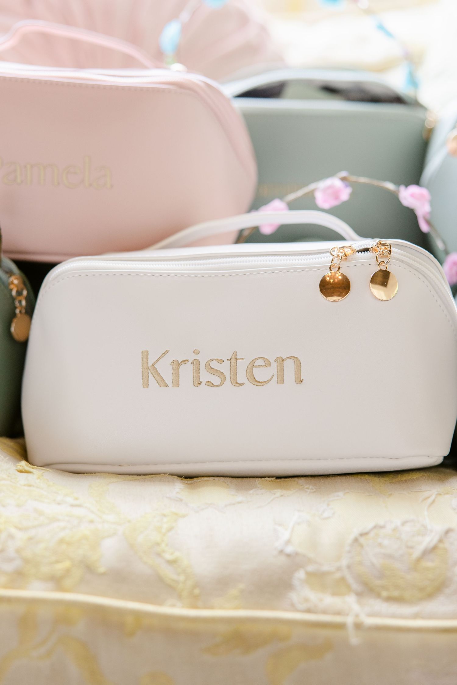 White sunglasses case with gold text spelling 'Kristen' and decorative earrings displayed on cream colored surface.