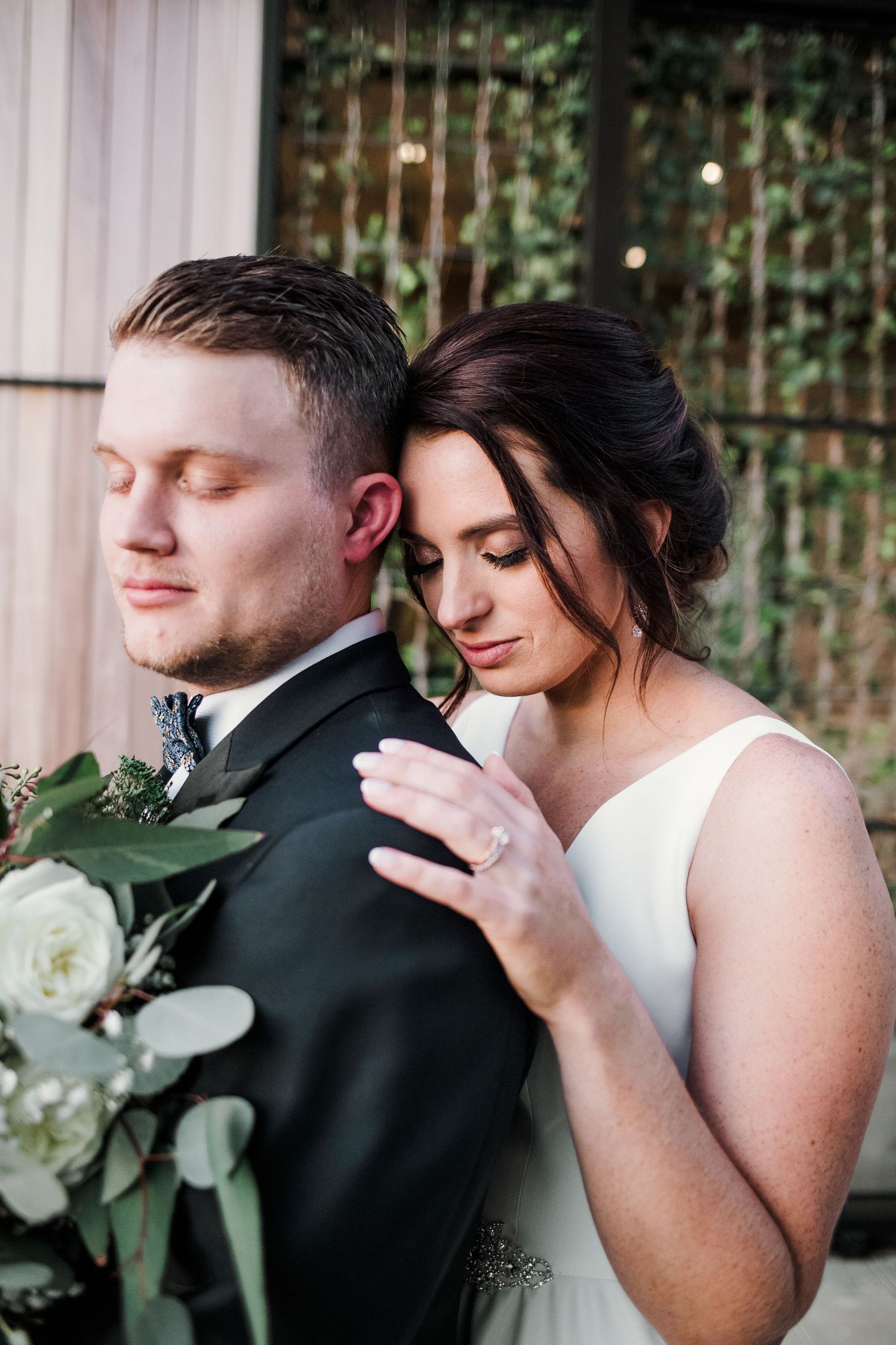 An intimate wedding moment captured between newlyweds with white roses and greenery bouquet.