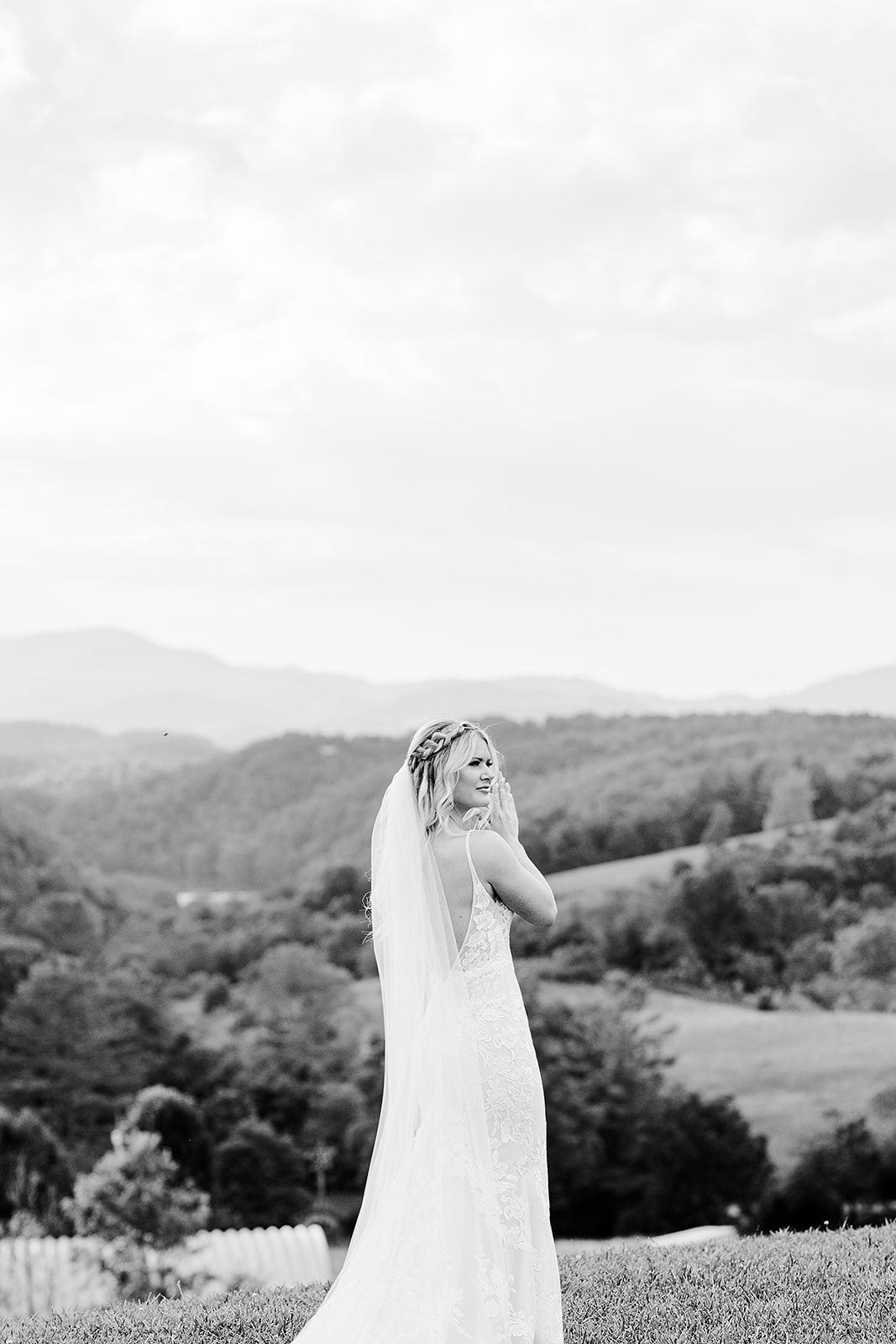 Black and white photograph of bride silhouetted against rolling mountain landscape.