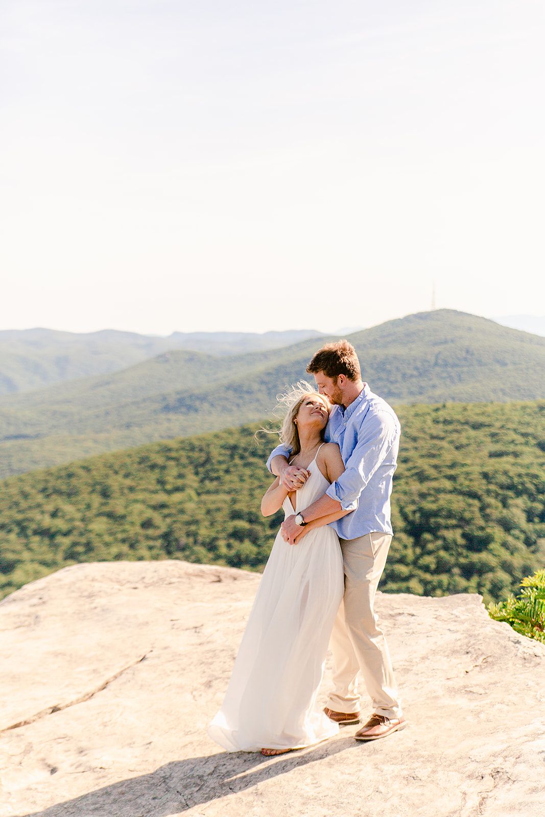 A romantic couple shares an intimate moment atop a scenic mountain overlook during their wedding photoshoot.