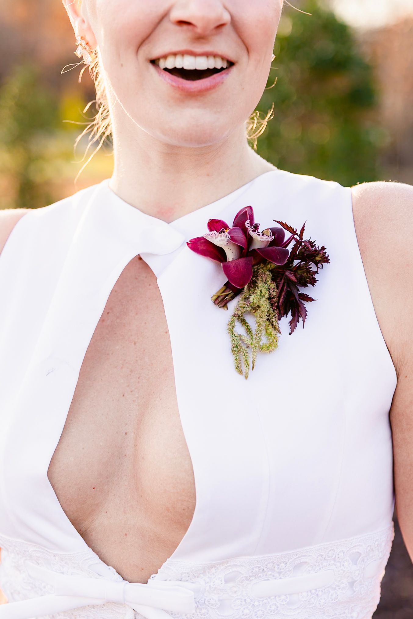 A burgundy floral corsage adorns a white dress with a stylish cutout detail.