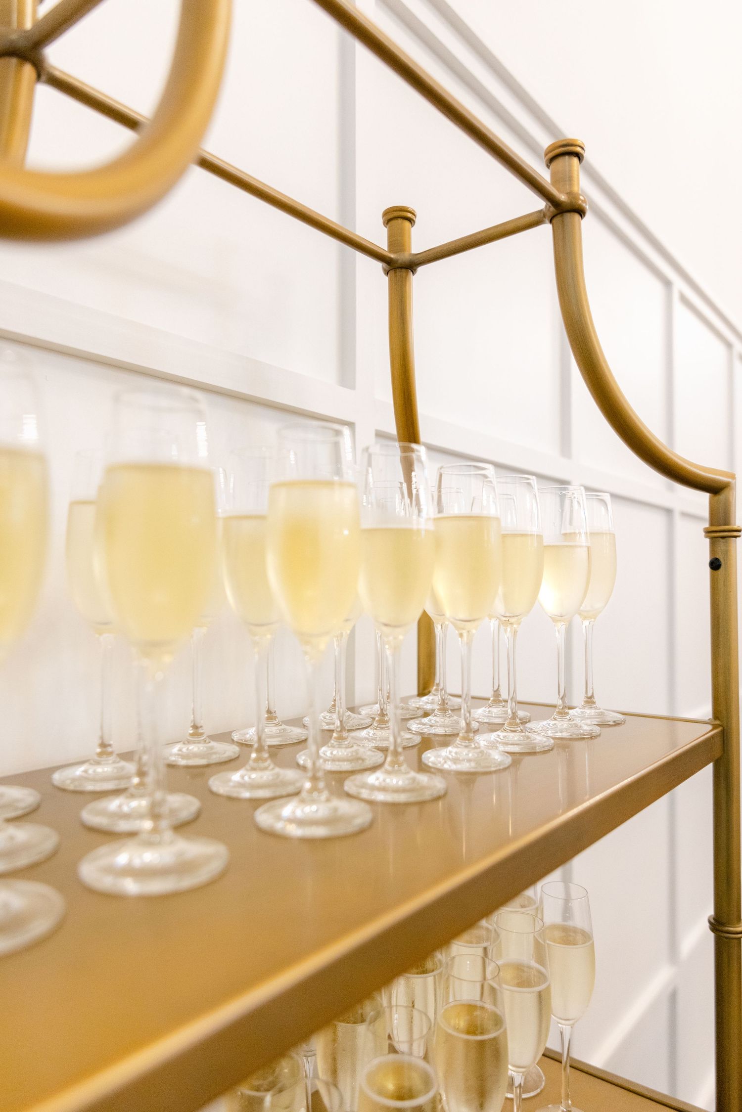 Gold bar cart displaying rows of champagne flutes filled with light-colored cocktails.