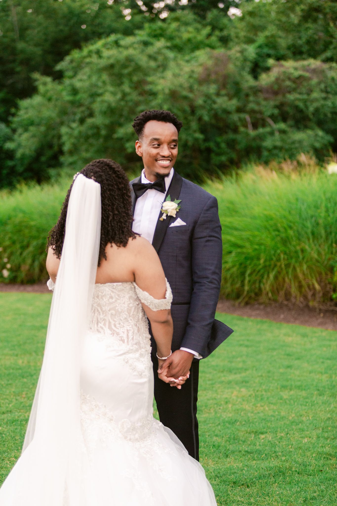 A joyful wedding couple shares a tender moment on manicured grounds with natural greenery.