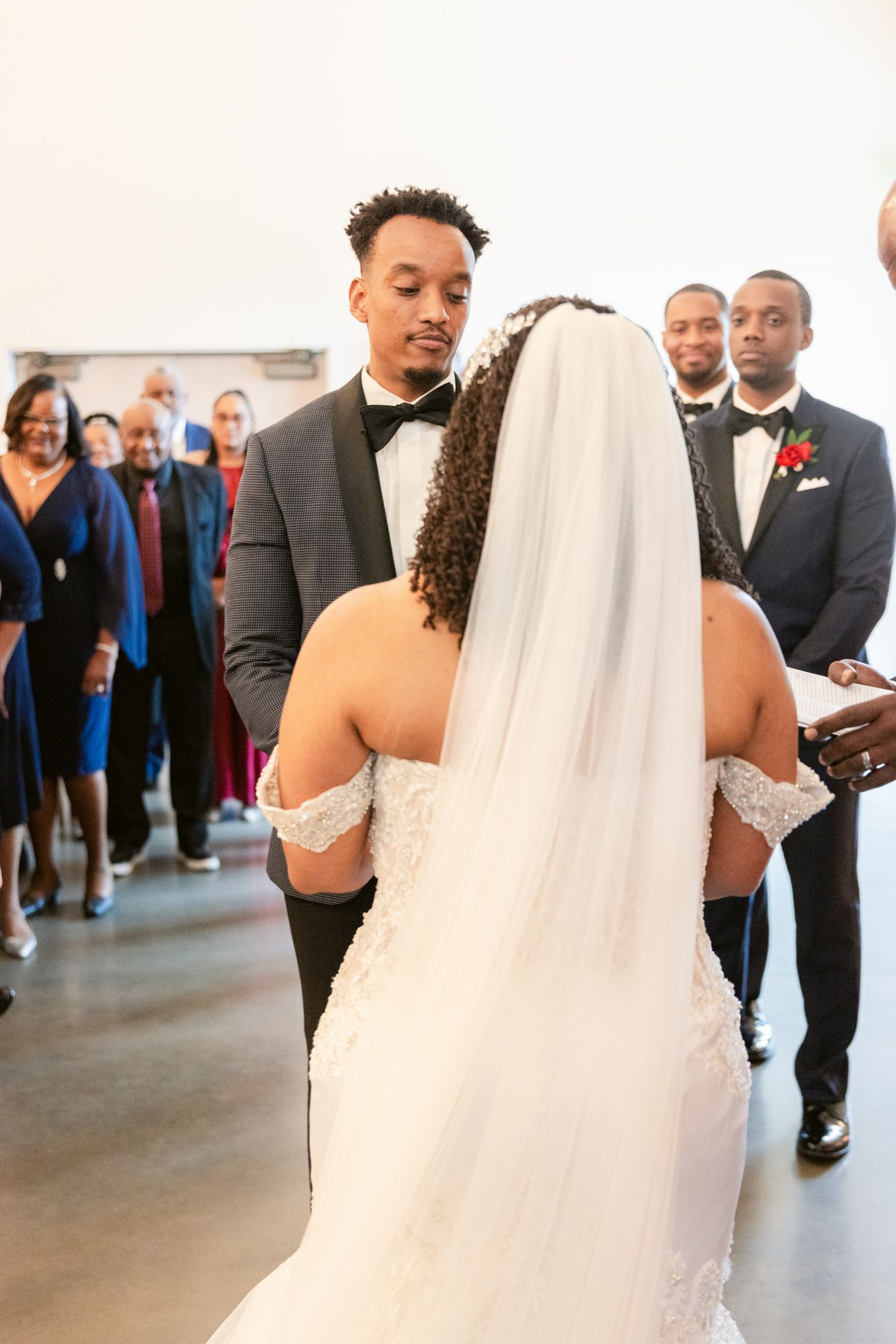 A couple exchanges vows during their wedding ceremony while guests look on in a modern indoor venue.