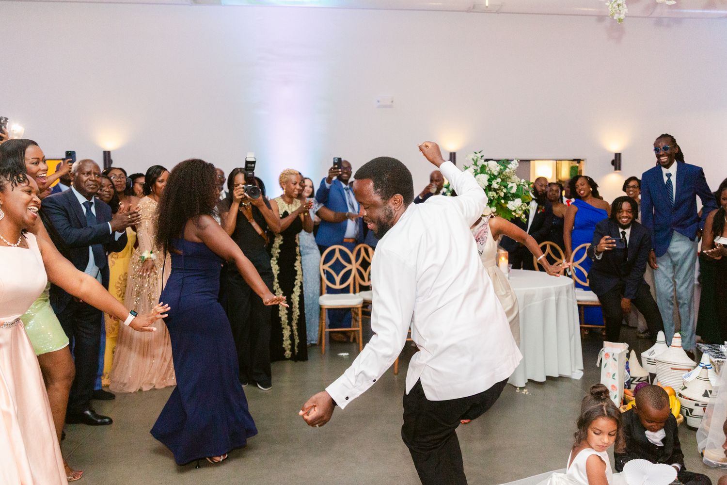 Guests enjoying themselves at a wedding reception with people dancing in a white-walled venue.