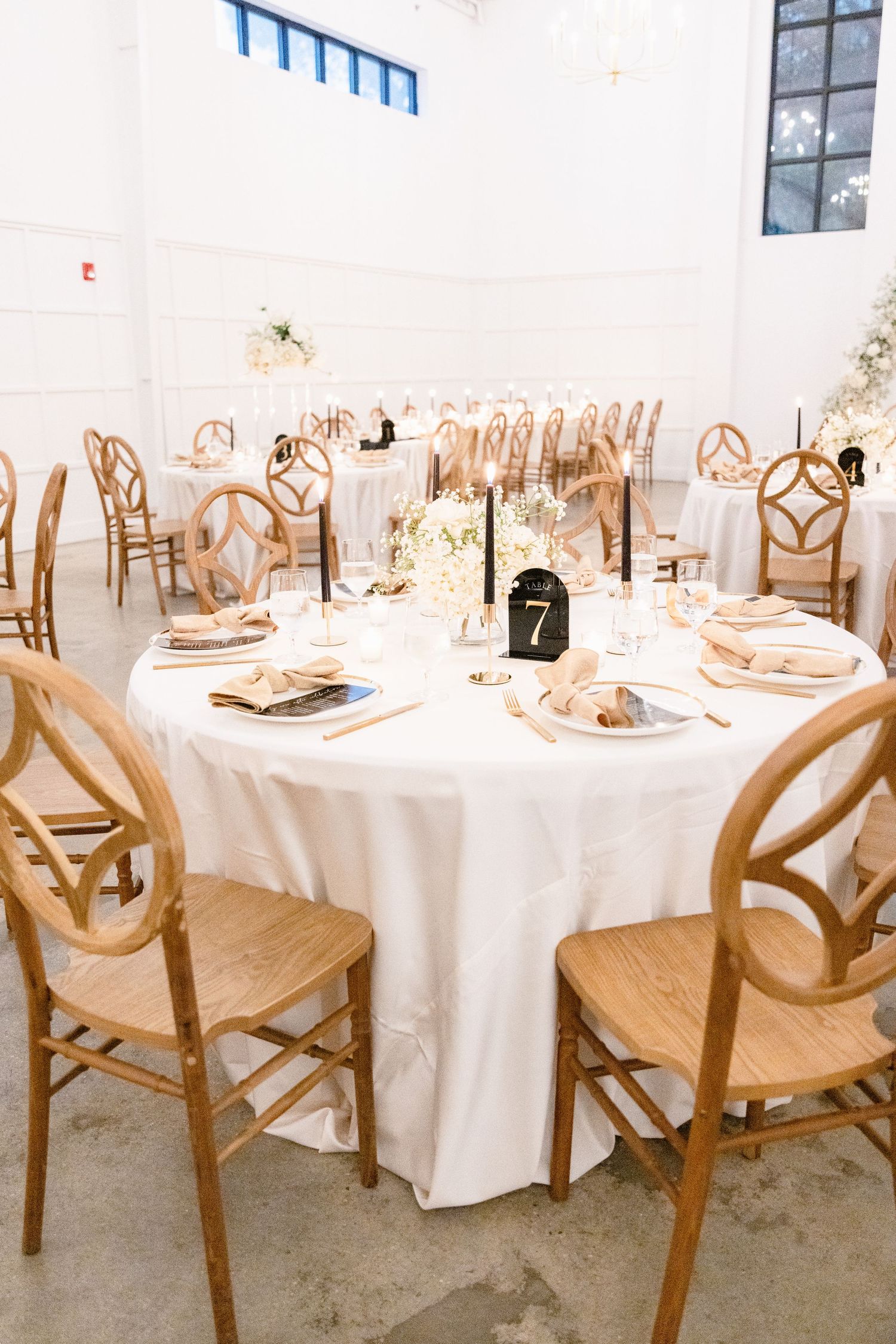 Elegant wedding reception table setup with white linens and wooden chairs featuring table number seven.