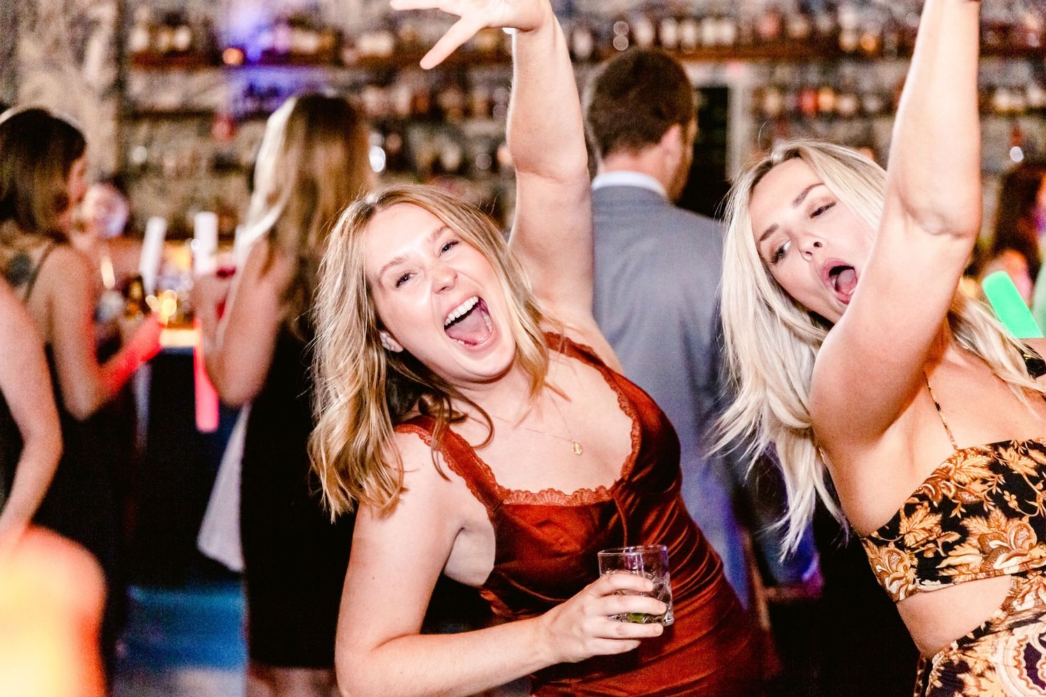 People dancing and celebrating together at a lively bar or party venue with colorful lighting in the background.