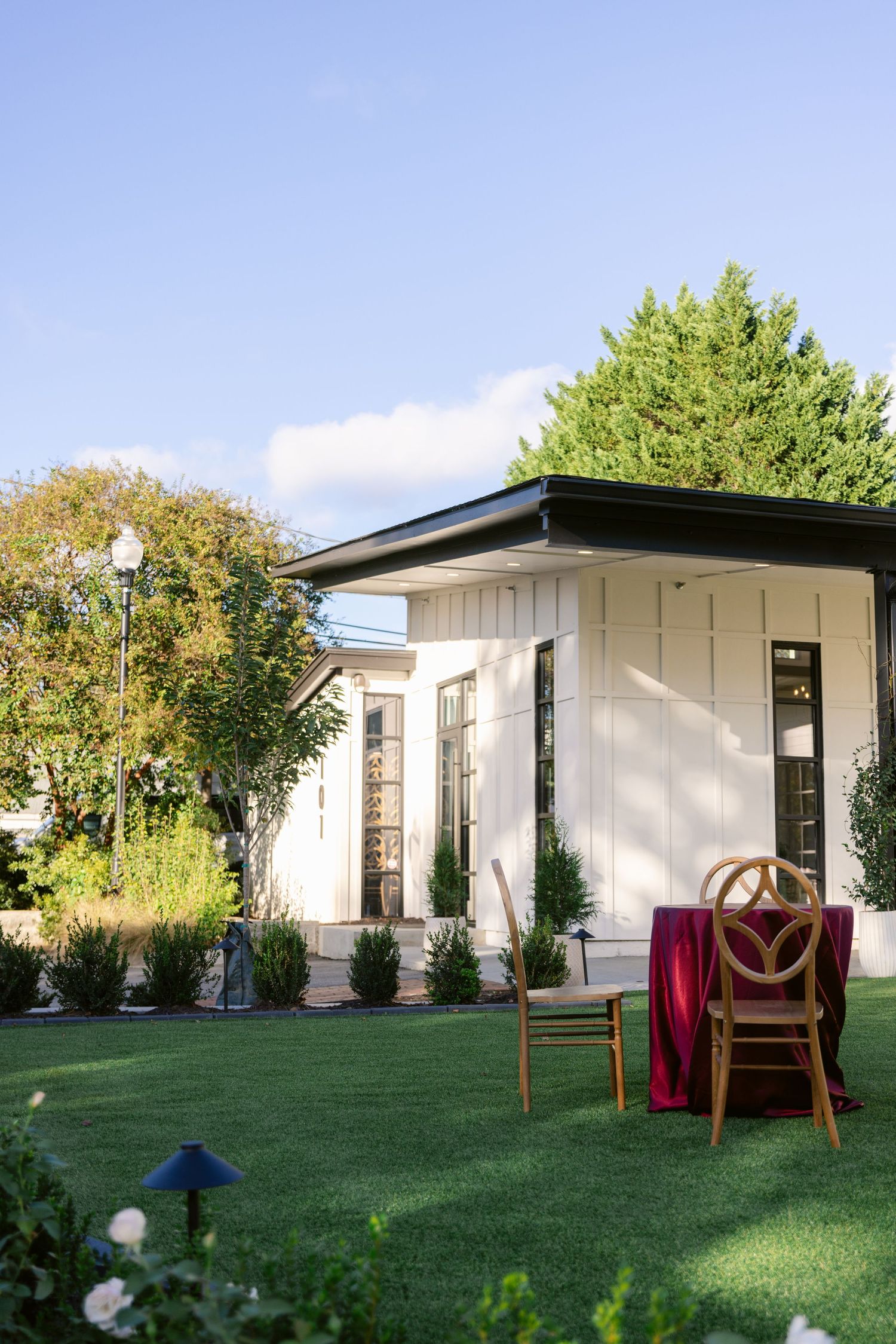 Modern white modular home with large windows and covered patio area set on a green lawn with trees in the background.