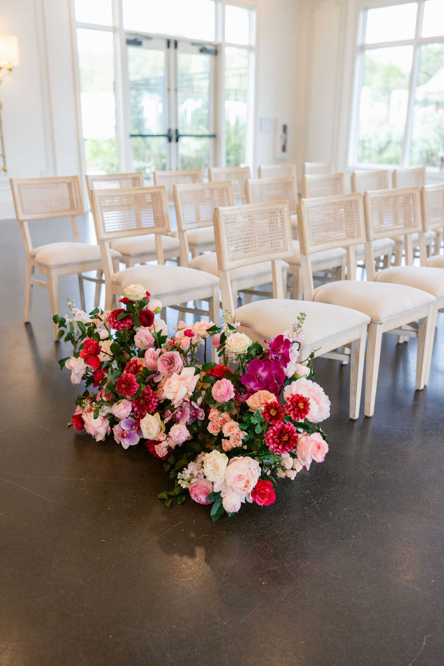 White ceremony chairs arranged with vibrant pink and red floral aisle decorations.