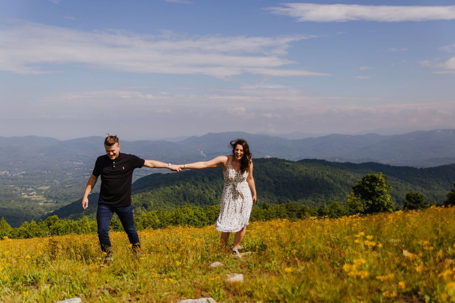 Playful couple holds hands while dancing in a mountain meadow filled with yellow wildflowers.