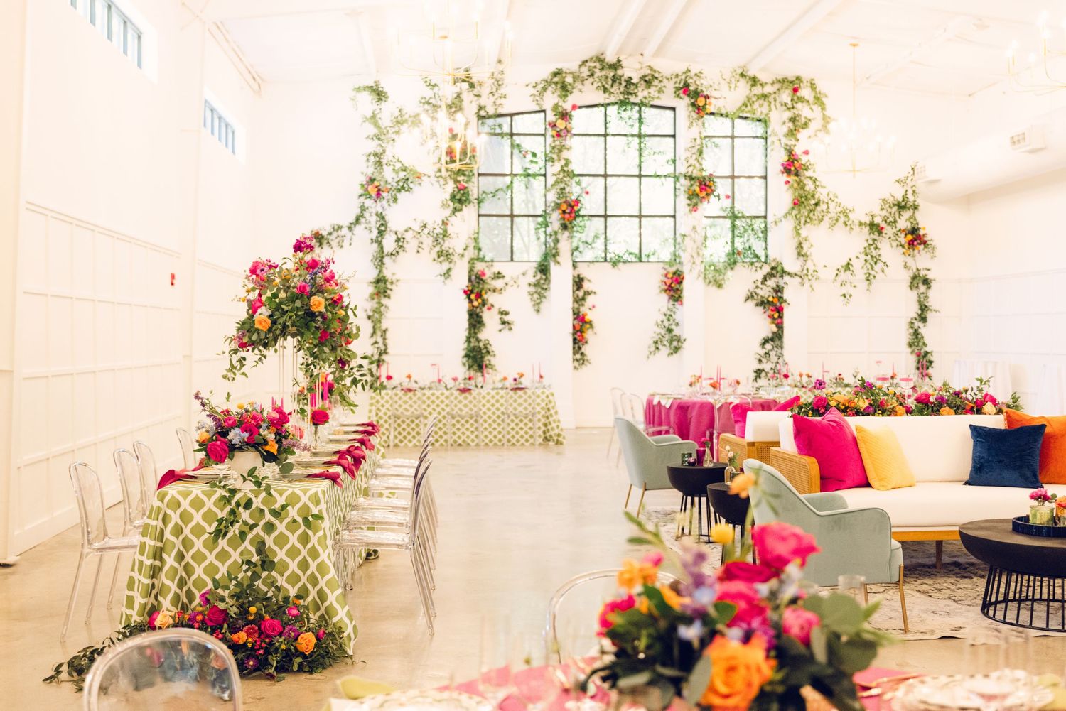 White event space decorated with hanging greenery, lattice panels, and colorful floral accents.