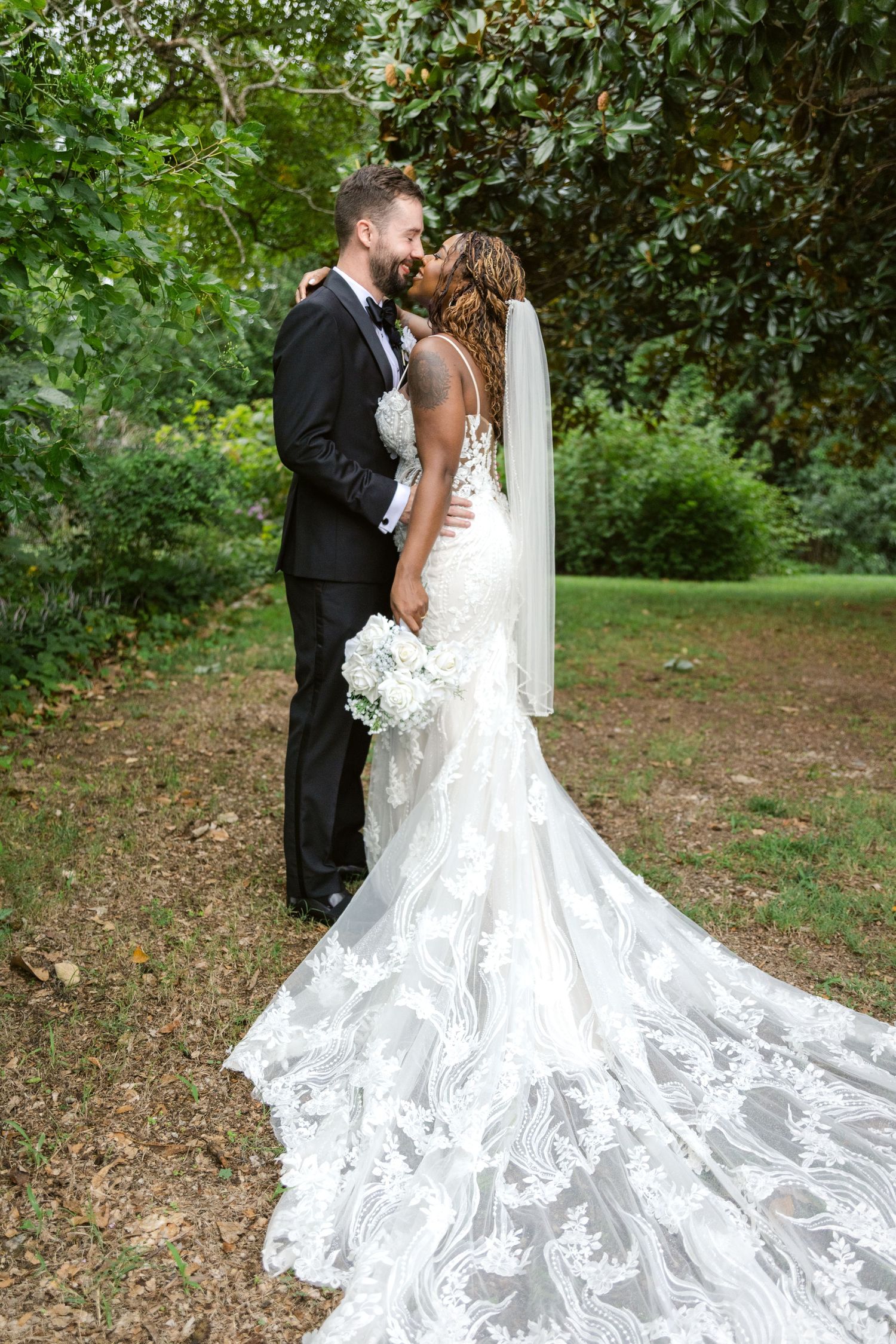 A romantic wedding portrait showing the dramatic sweep of a lace wedding gown train in a garden setting.