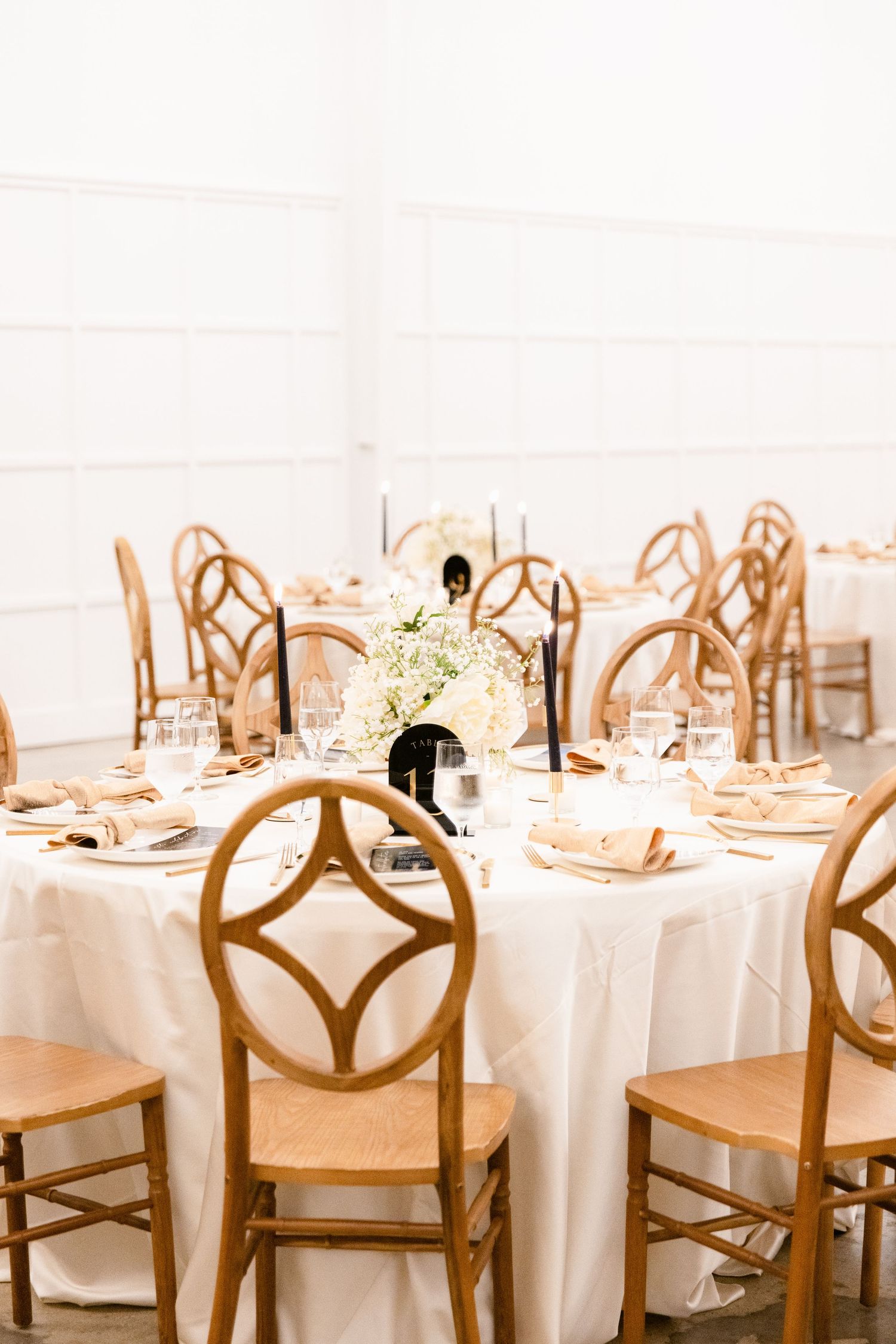 Banquet hall setup with white tablecloths and wooden cross-back chairs.