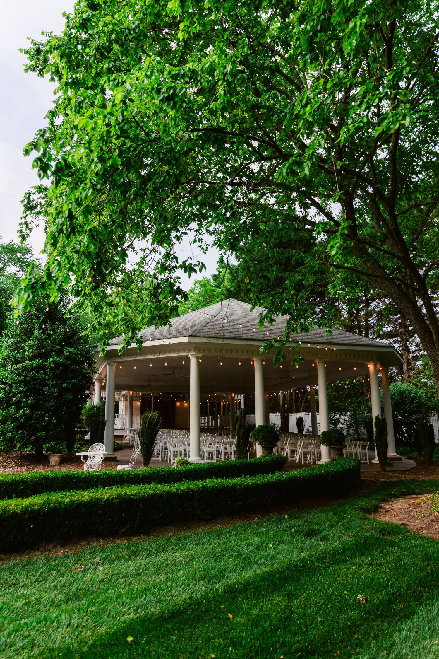Panoramic view of white building with covered porches nestled among green trees on sloping lawn.