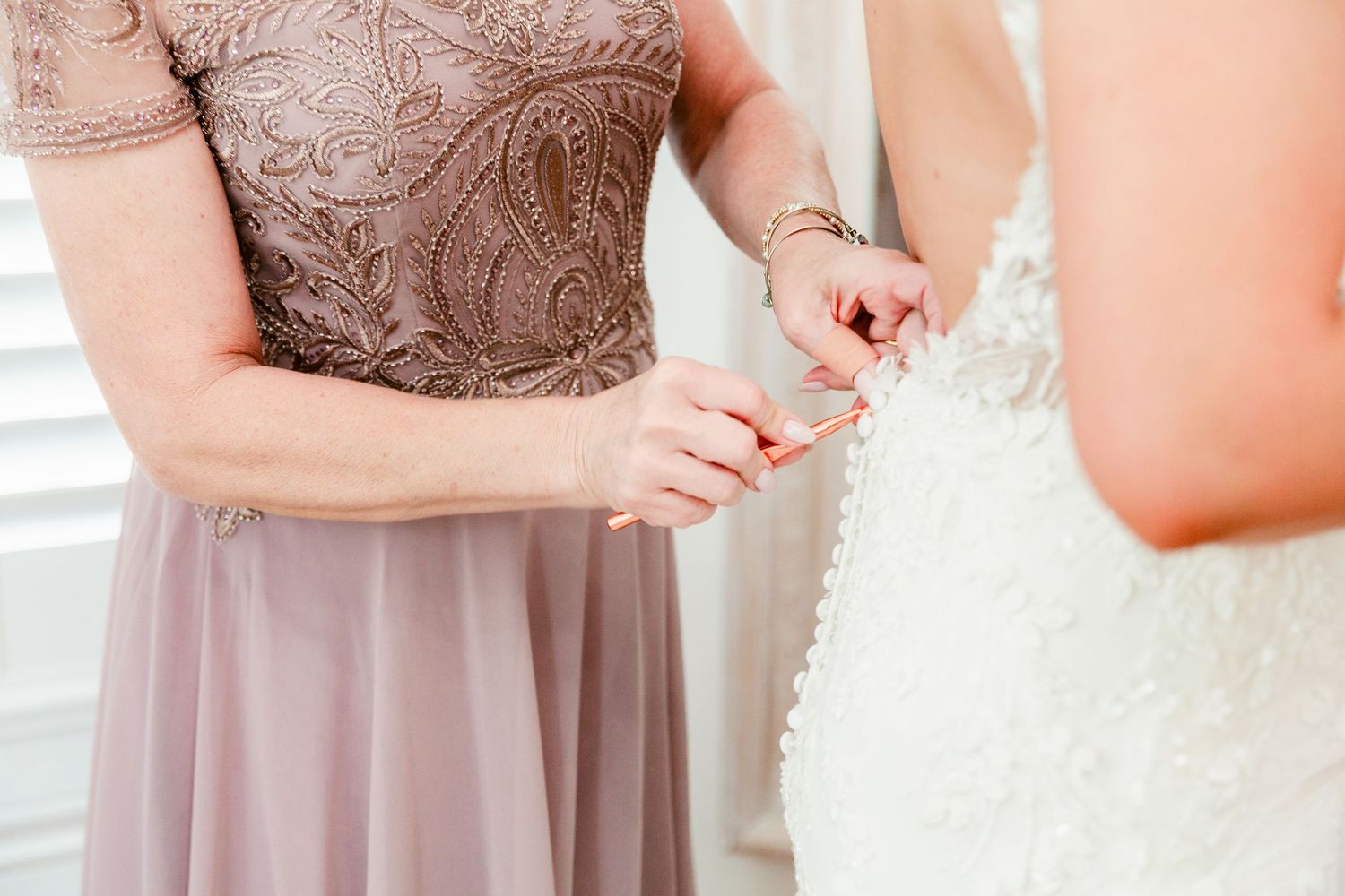 Bridesmaids in soft mauve dresses stand together while helping adjust the bride's white wedding gown.