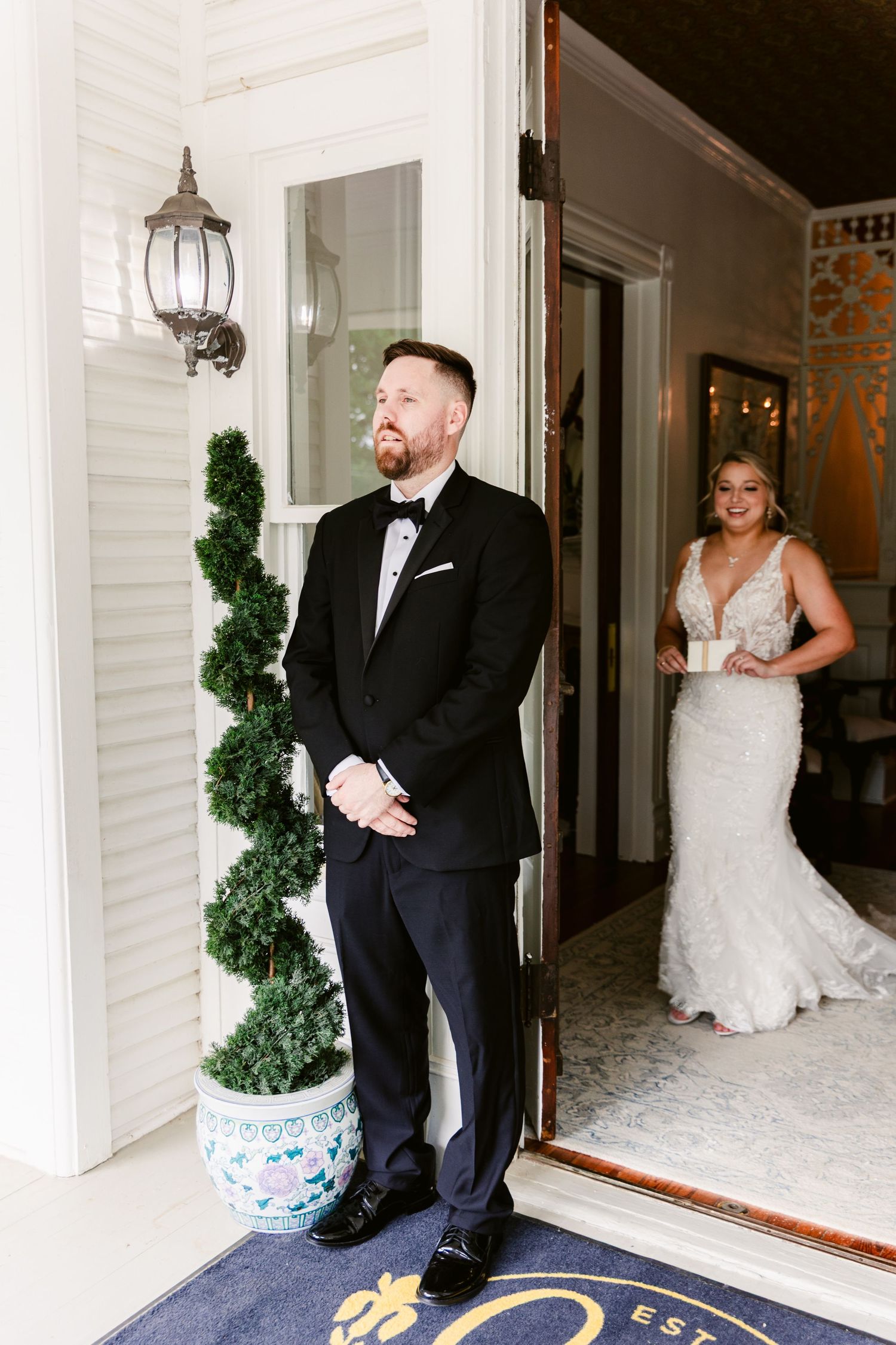 A couple shares a first look moment before their wedding ceremony, with the bride peeking from behind a doorway.