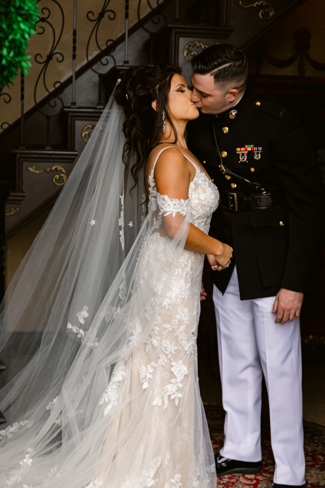 A romantic wedding moment captured on an ornate staircase with the bride wearing a lace gown with flowing veil.