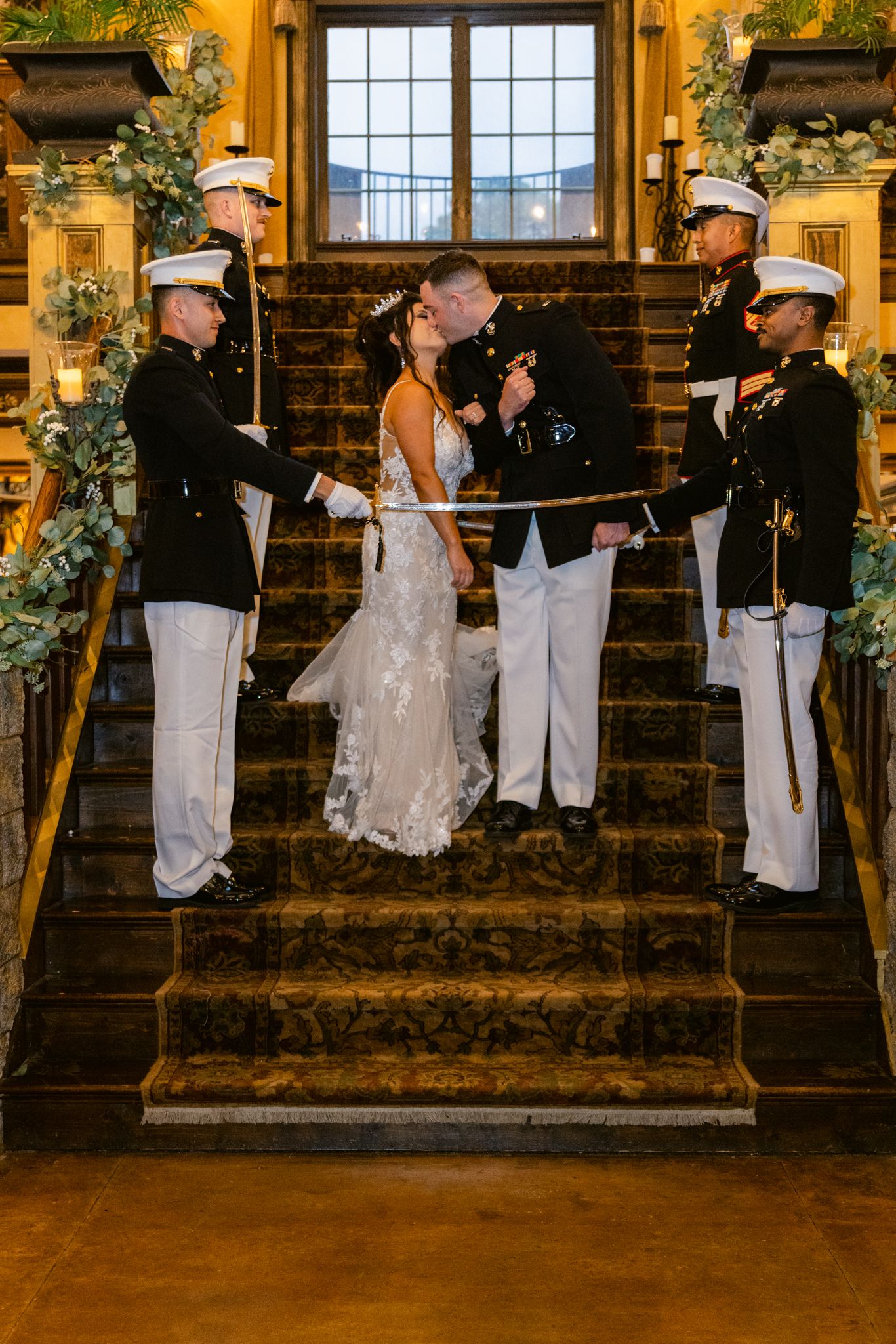 Wedding party poses on rustic stone steps decorated with greenery and illuminated by warm evening lighting.