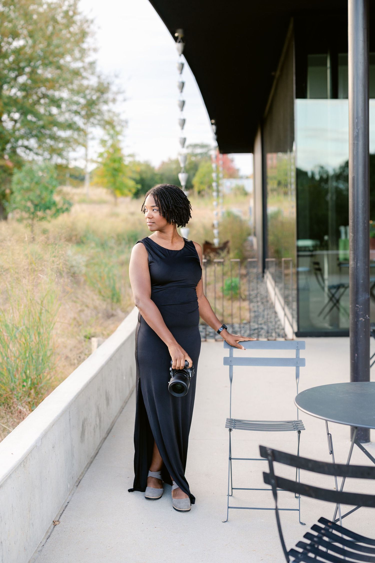 A person in a navy dress sits thoughtfully on a modern patio with white walls and blue chairs.
