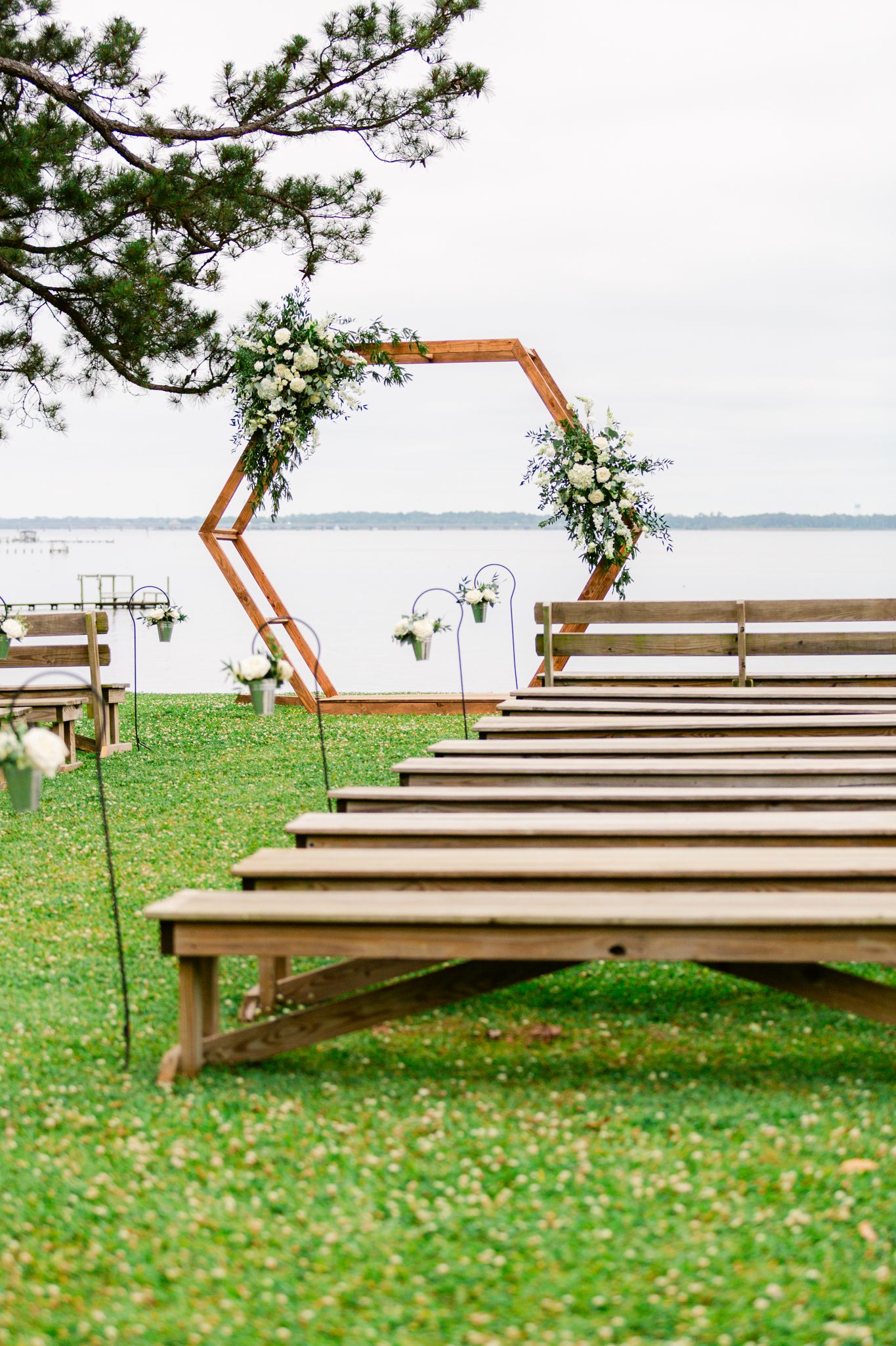 Modern wooden benches arranged in rows on a grassy hillside overlooking a serene lake view with pine trees above.
