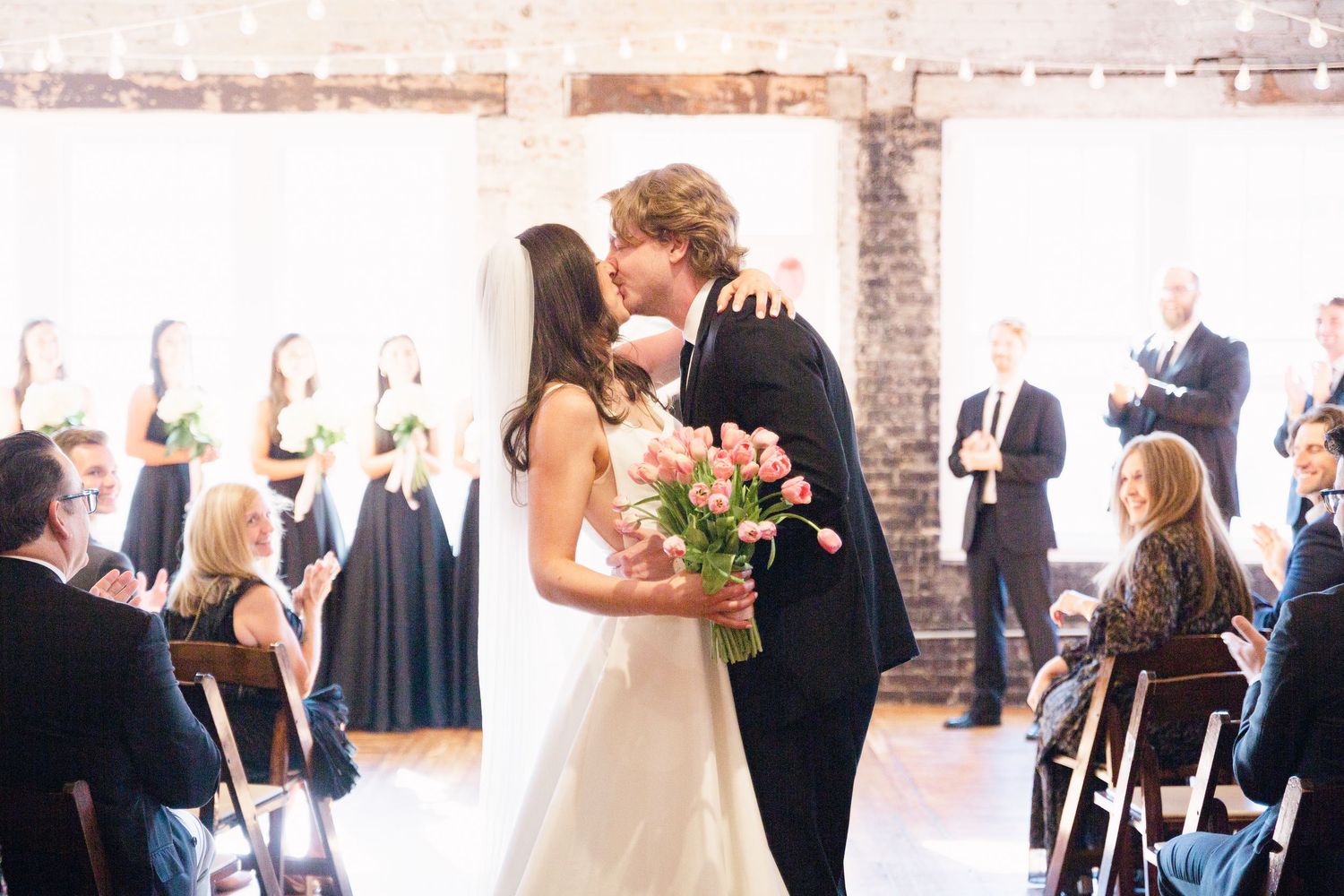 A wedding ceremony kiss moment in an indoor venue with exposed brick walls.