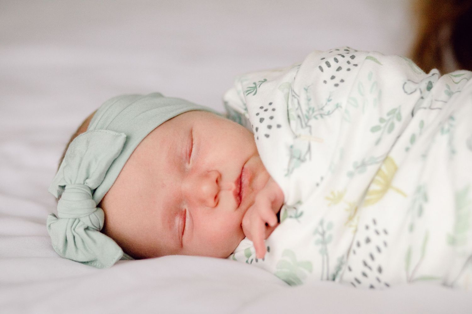 Peaceful newborn baby sleeping in soft white bedding with mint green accents.