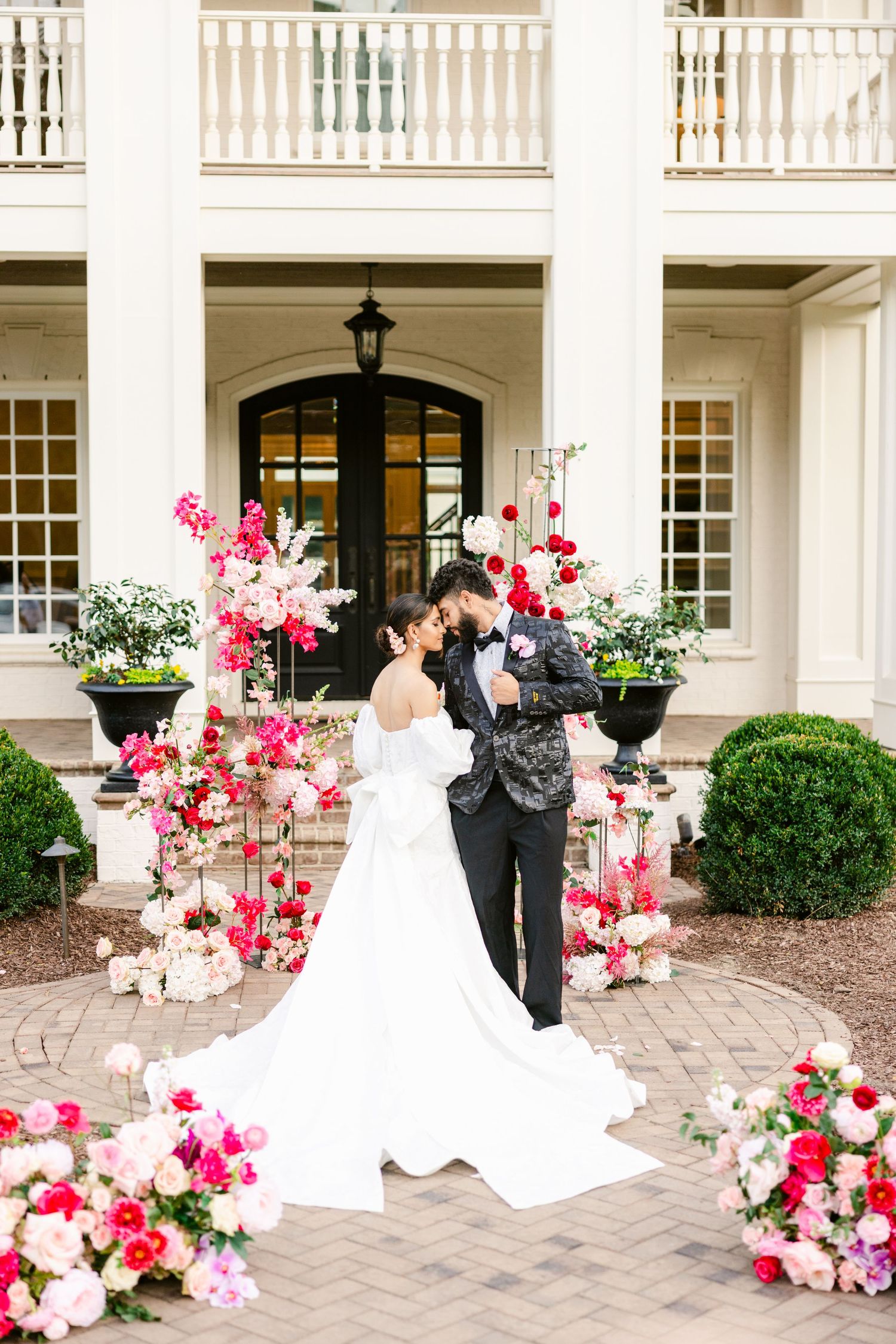Wedding couple posing on brick patio with pink and red floral arrangements.