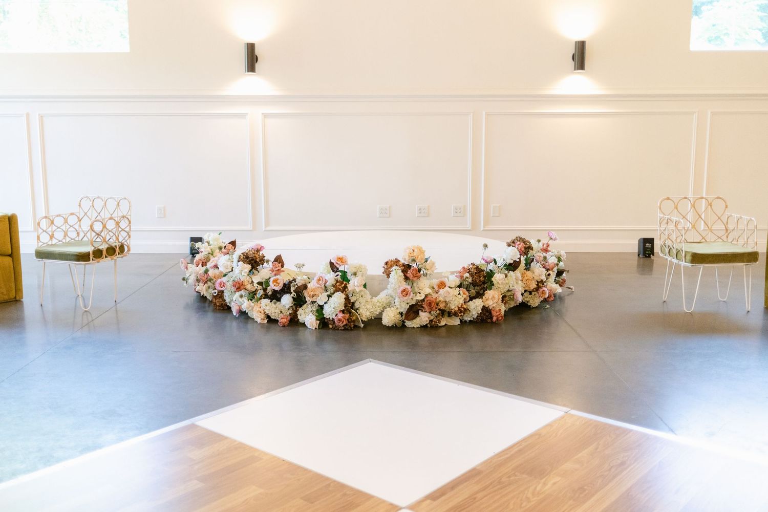 A modern white ballroom with elegant wainscoting, recessed lighting, and a decorative floral arrangement on display.