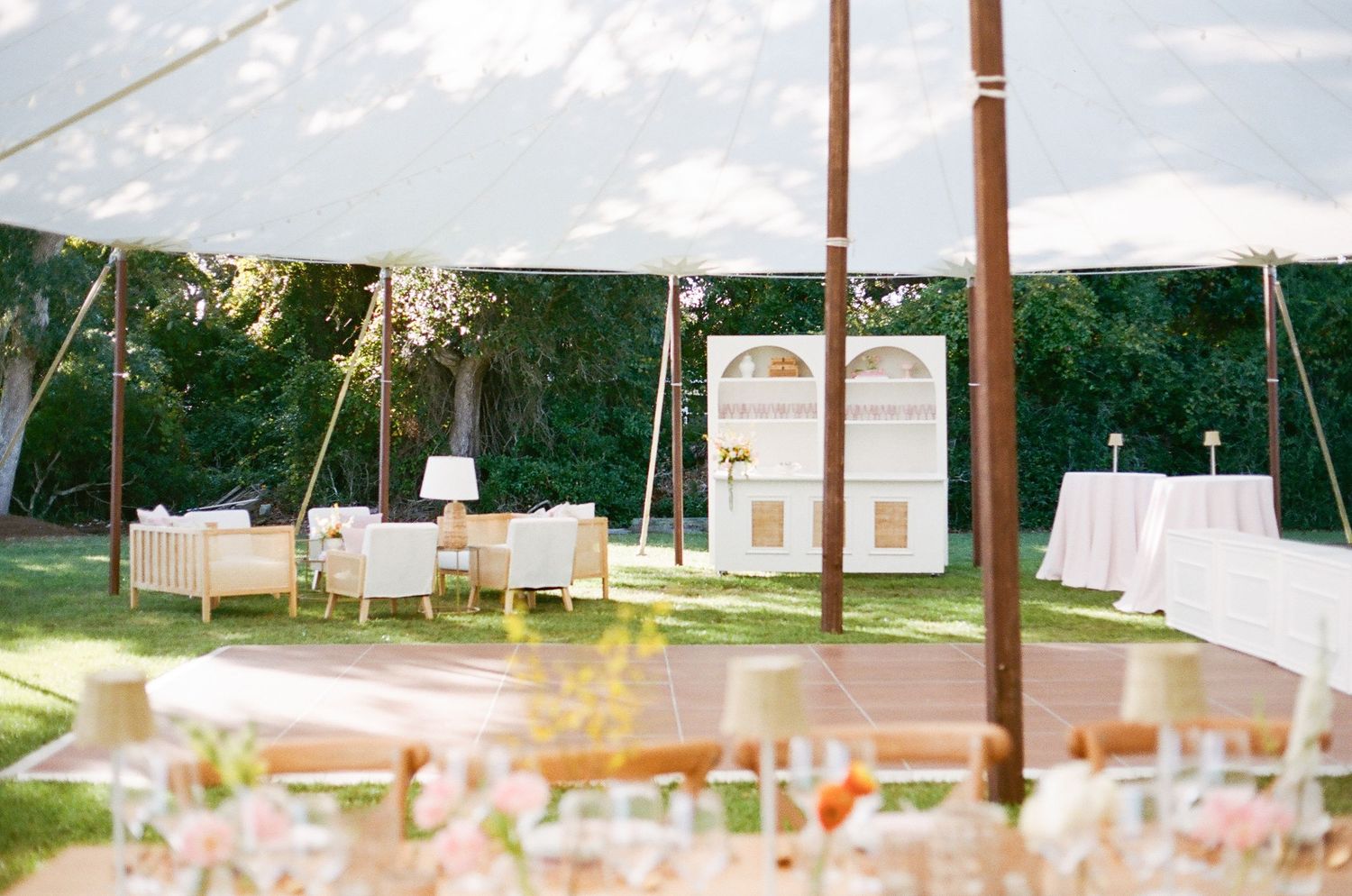 A row of elegant white wedding tents set up outdoors with decorative lighting and table settings visible inside.