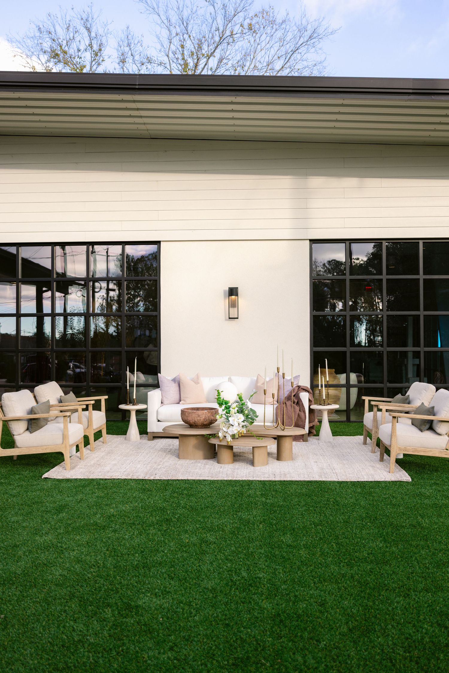 Modern white patio furniture arranged on concrete deck with lush green lawn and large windows of contemporary home.