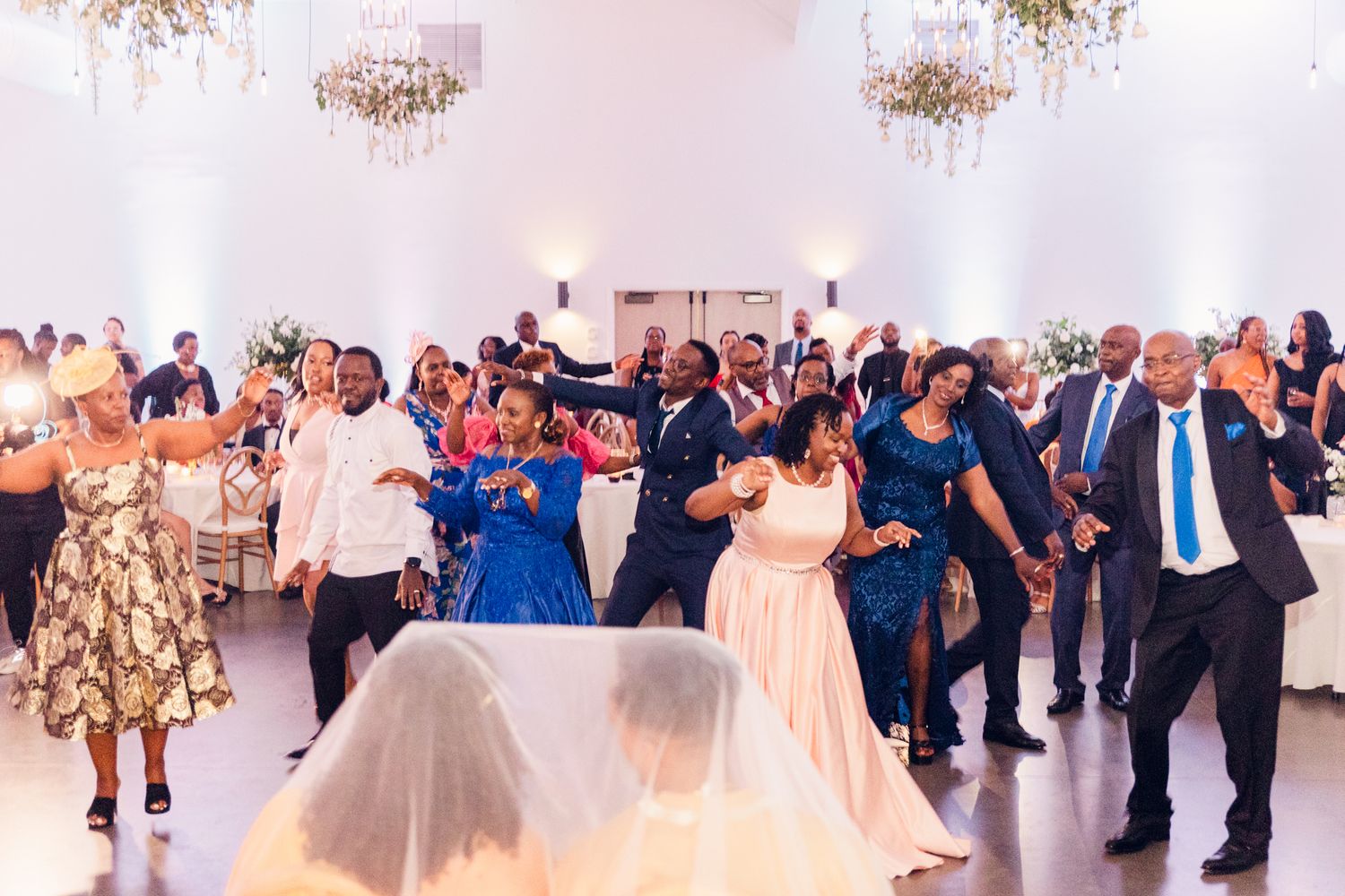 Panoramic view of wedding reception venue with chandelier and guests celebrating on dance floor.