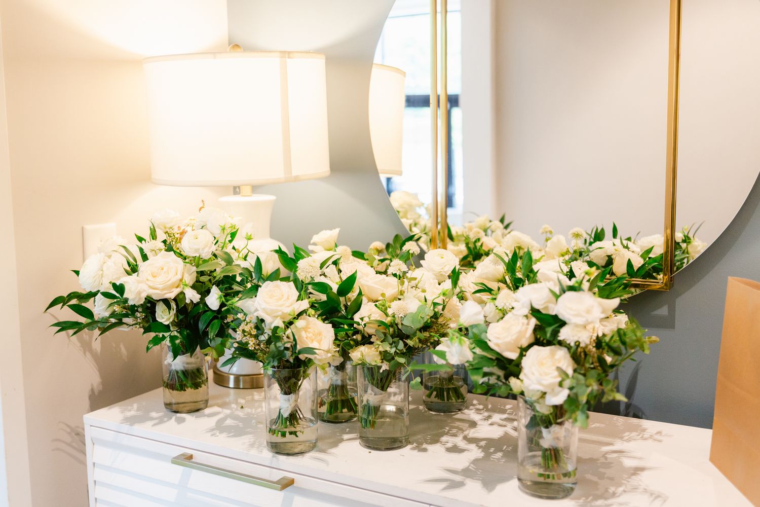 A long banquet table decorated with elegant white floral centerpieces and gold candlesticks in a bright, modern setting.