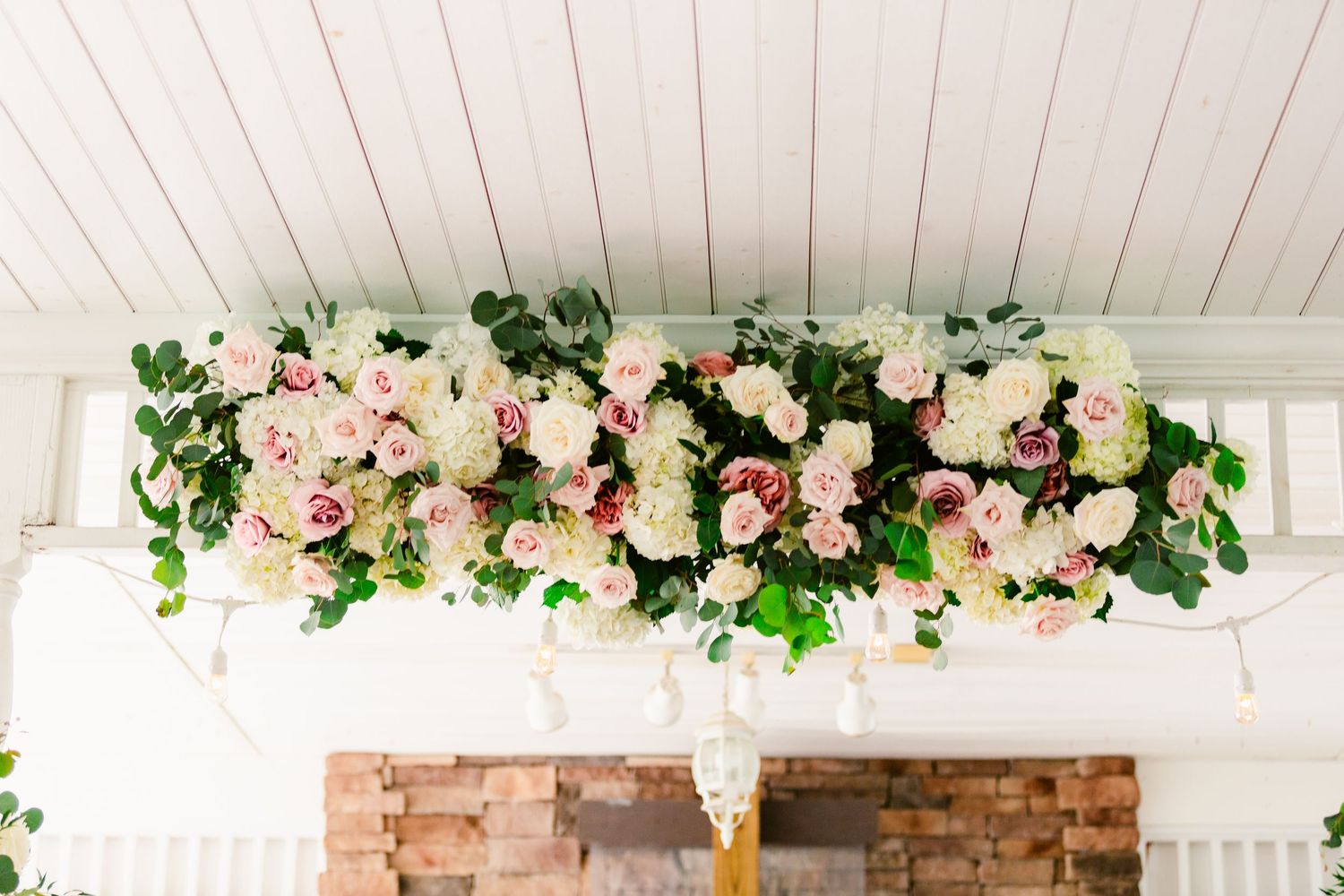 Romantic floral arch with pink roses and greenery adorns a brick ceremony backdrop.