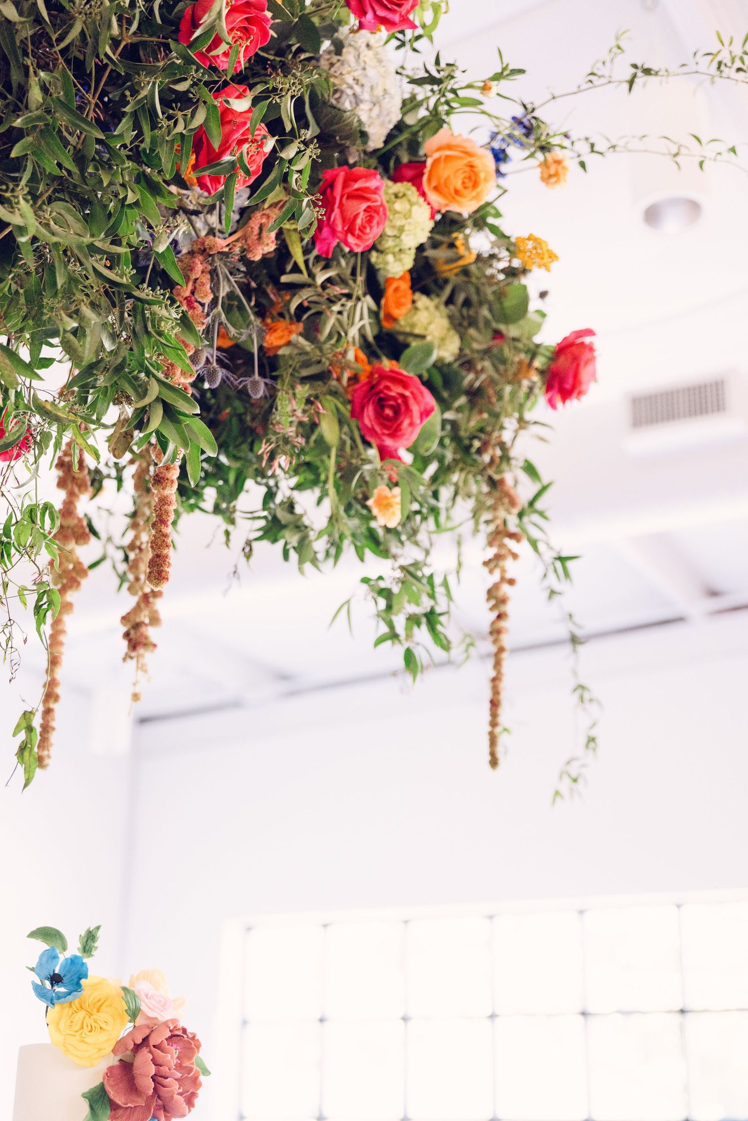 Elegant table setting with vibrant red and orange floral arrangements hanging from above at a wedding reception.