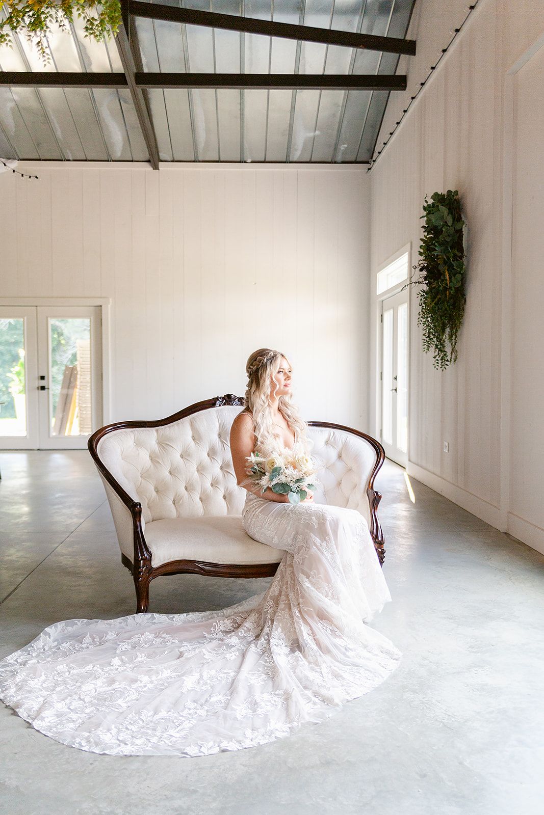 Wedding dress displayed on tufted settee in bright white studio space.