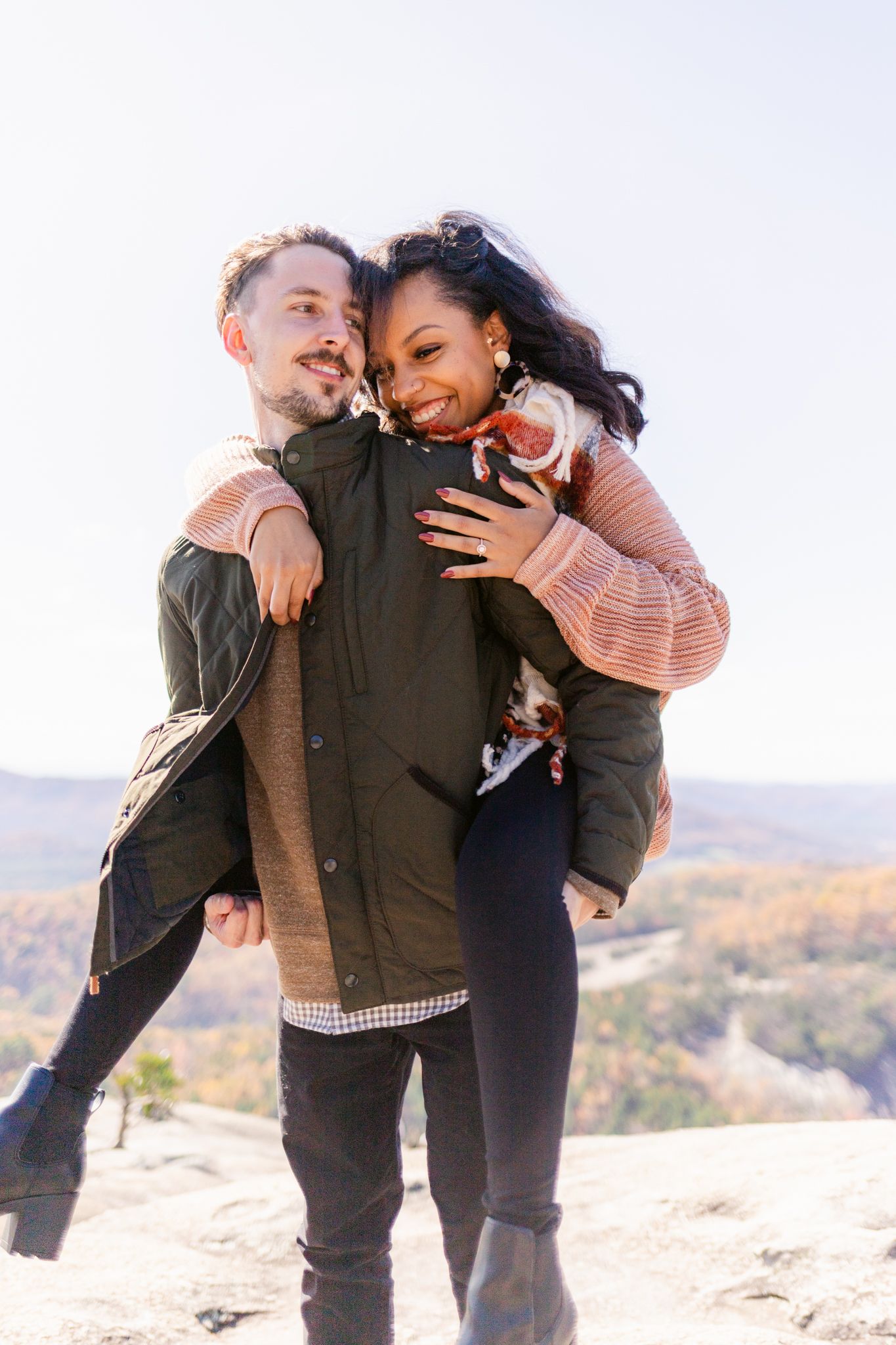 A couple shares playful and romantic moments while posing together on a rocky mountain overlook during autumn.