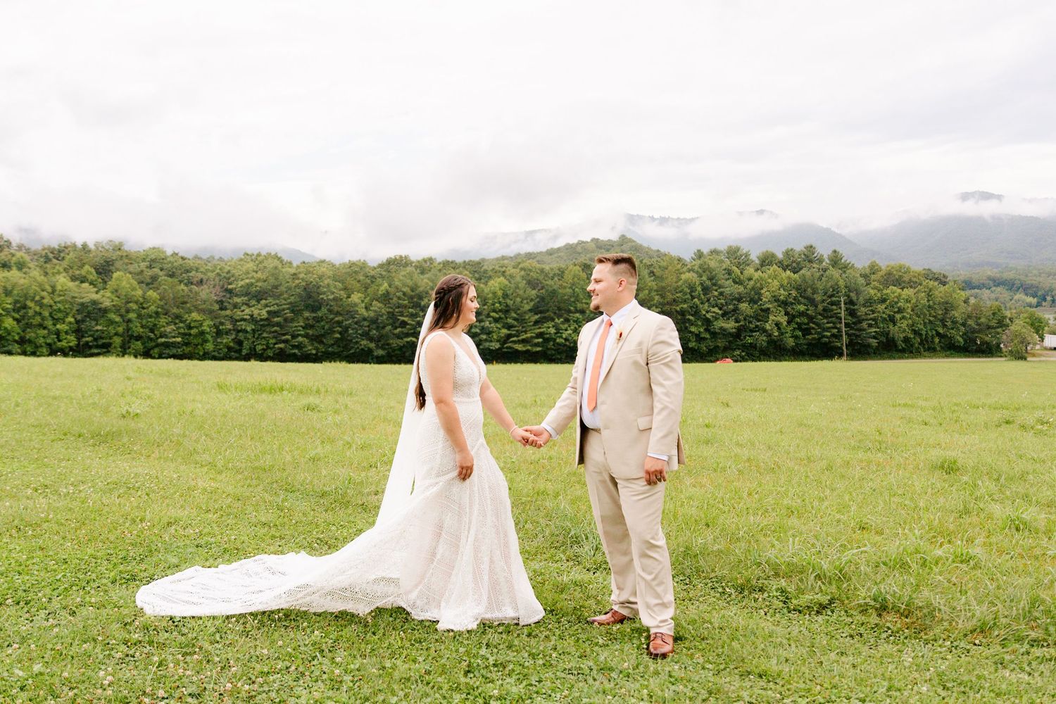 Panoramic view of a couple walking in a lush green field on their wedding day.