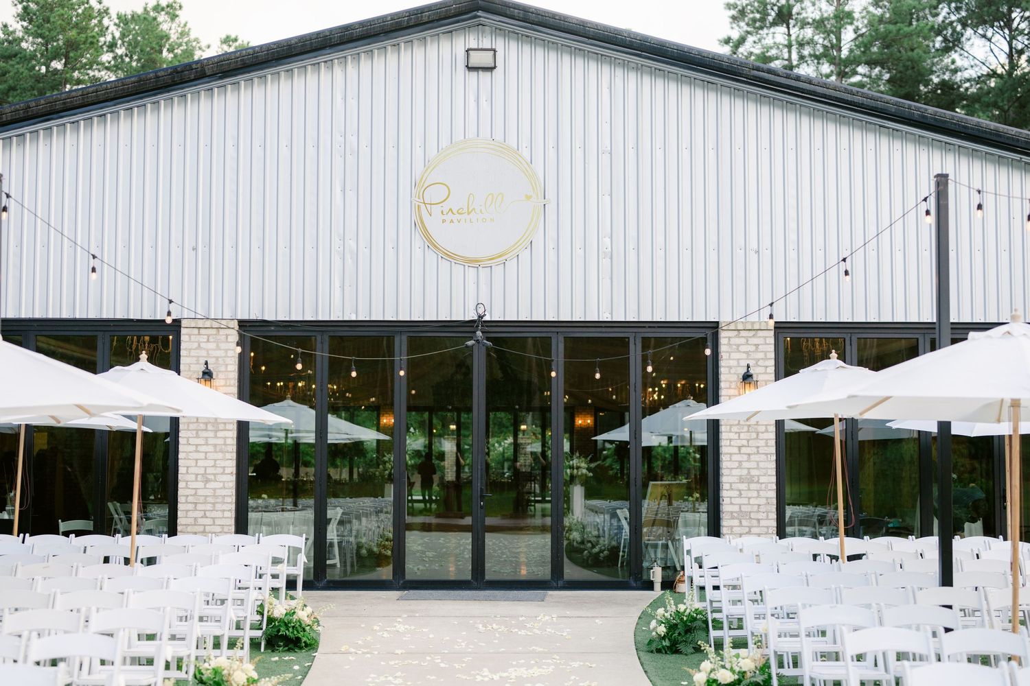Modern white pavilion with outdoor seating arranged for a wedding reception under a forest canopy.