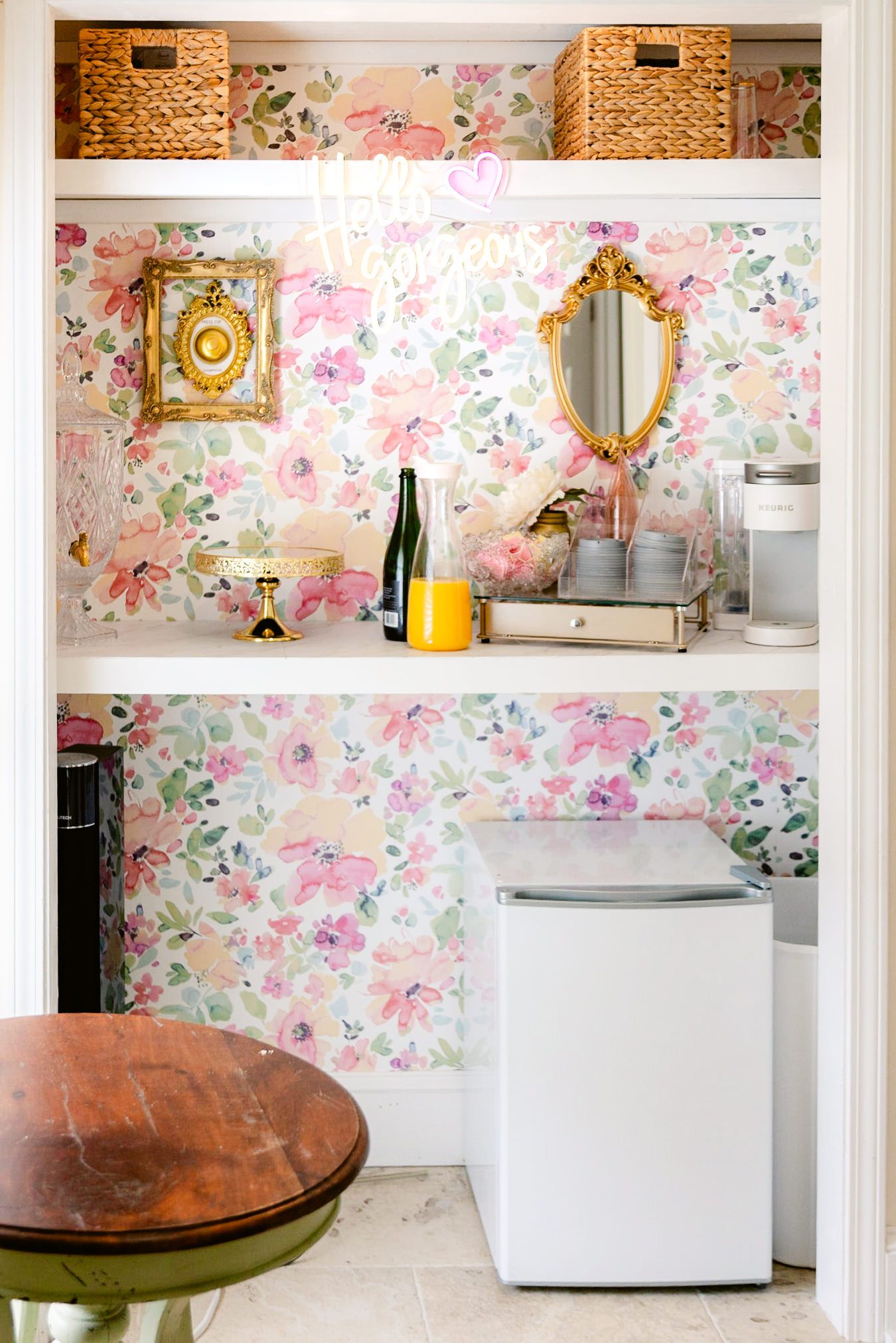 A kitchen space with floral wallpaper, wicker baskets, and a round wooden table visible in the corner.