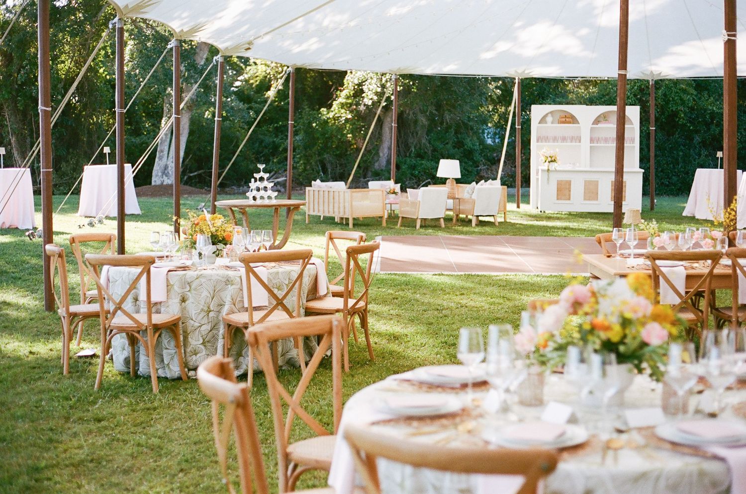 Elegant outdoor wedding reception setup with wooden cross-back chairs and white linens under string lights at sunset.