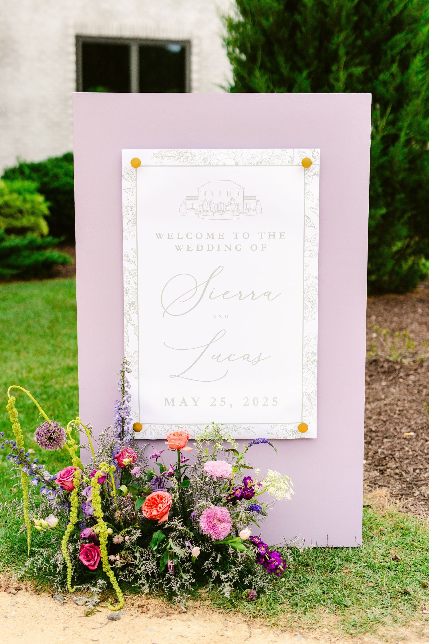 Wedding signage decorated with delicate wildflowers and greenery arranged along the bottom edge in a garden setting.