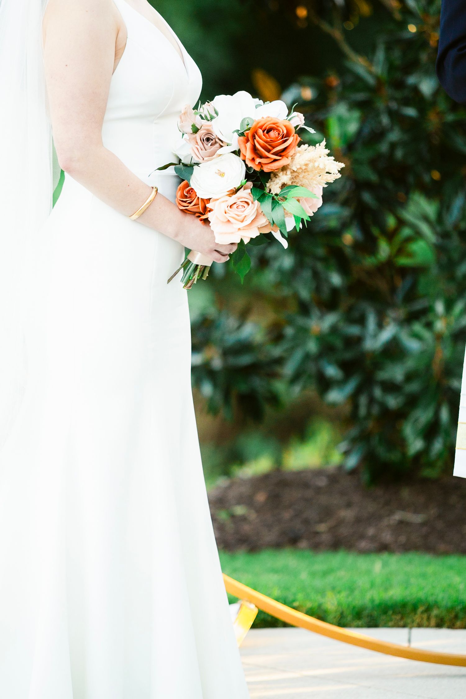 Wedding bouquet with peach and coral roses held against a white bridal gown outdoors.