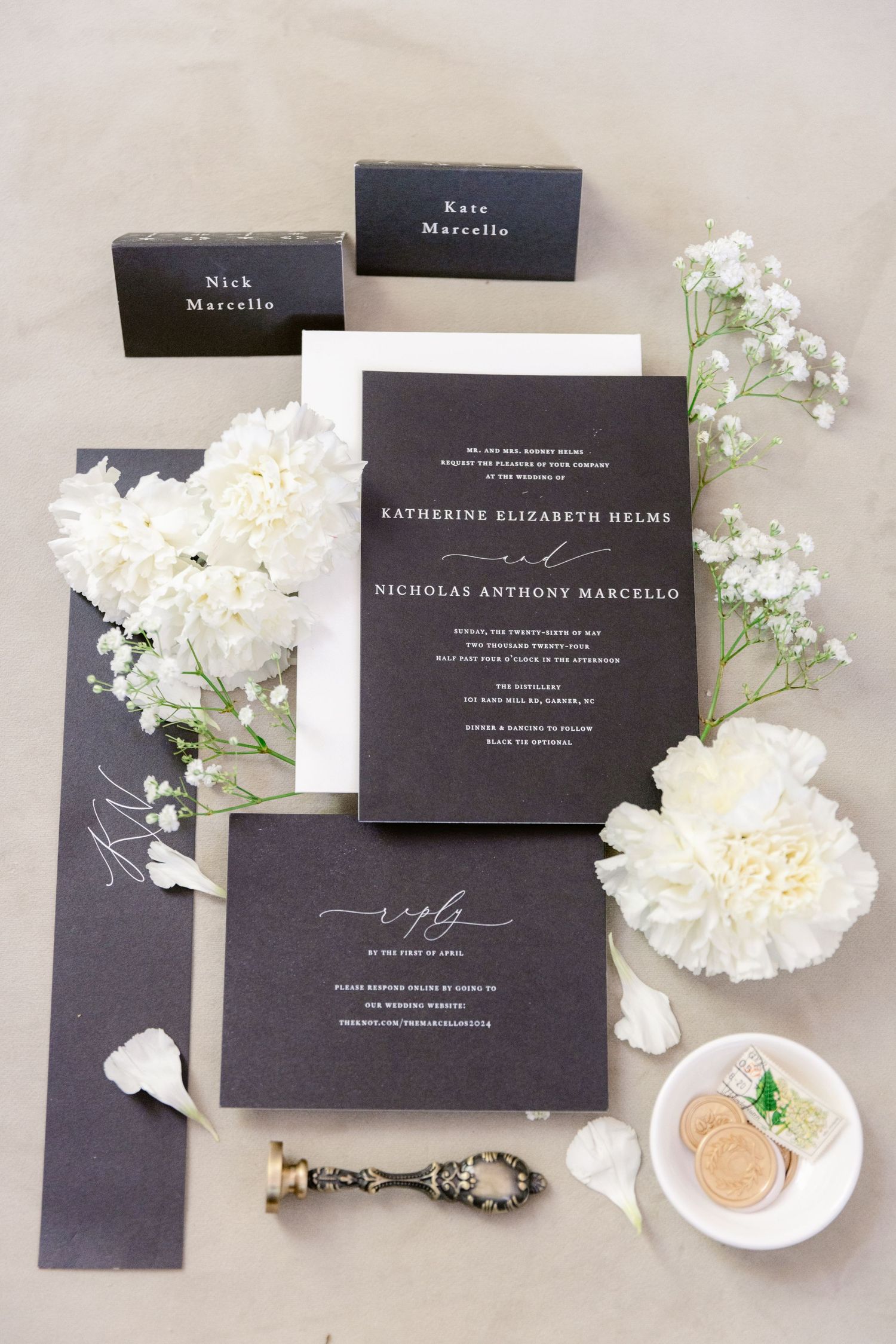 Elegant black and white wedding invitation suite with white flowers and place cards on light gray surface.