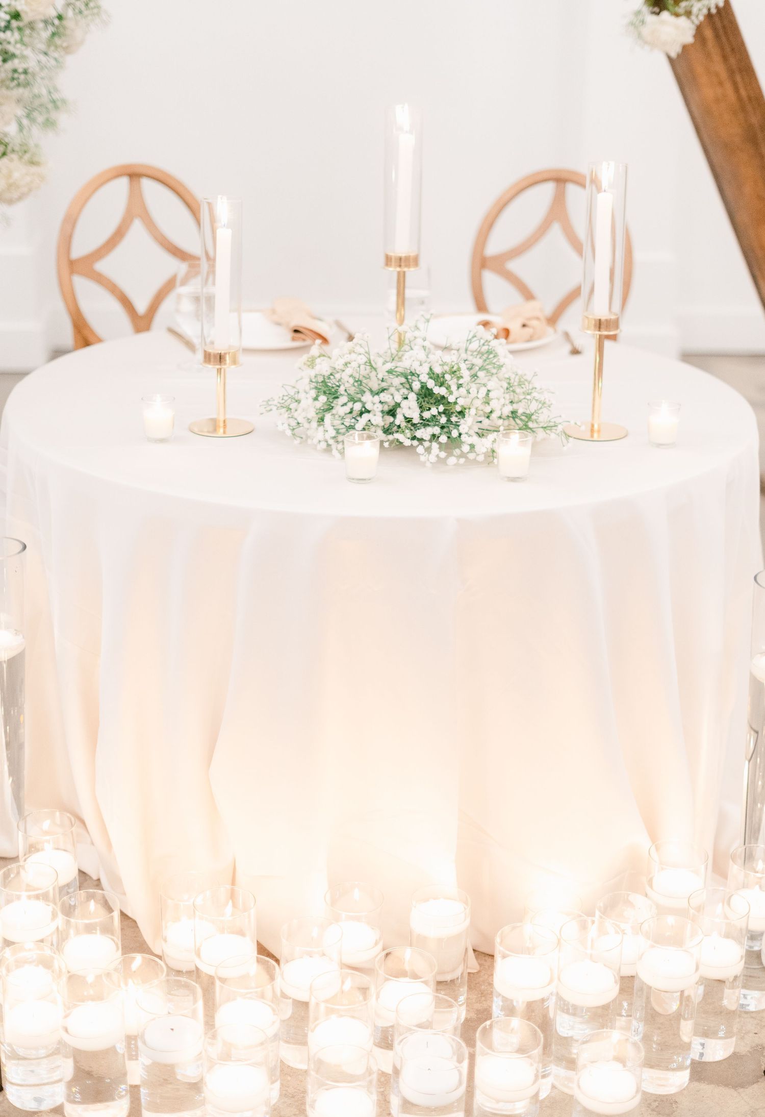 Elegant wedding reception tables set with white linens, gold chairs, and delicate floral arrangements in a light-filled venue.