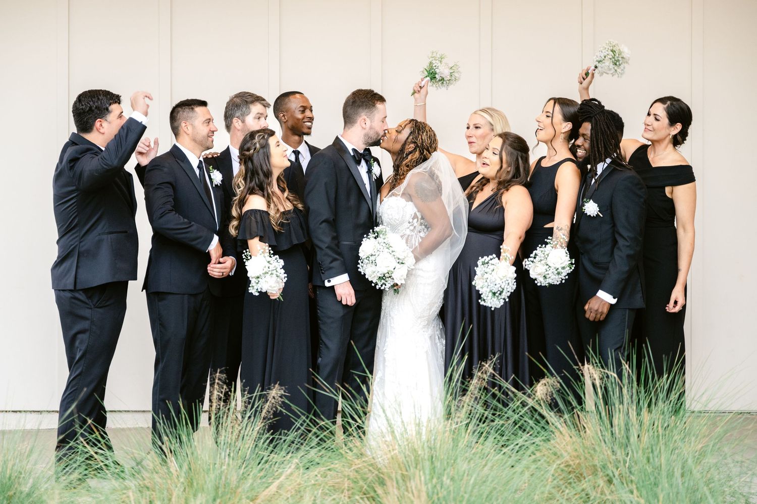 Wedding party stands in line outdoors laughing and looking up at something in the sky together.