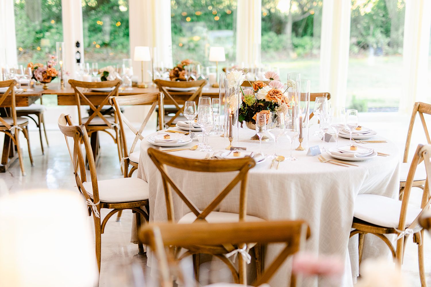 Light-filled reception space with round and rectangular tables set with white linens and wooden chairs.