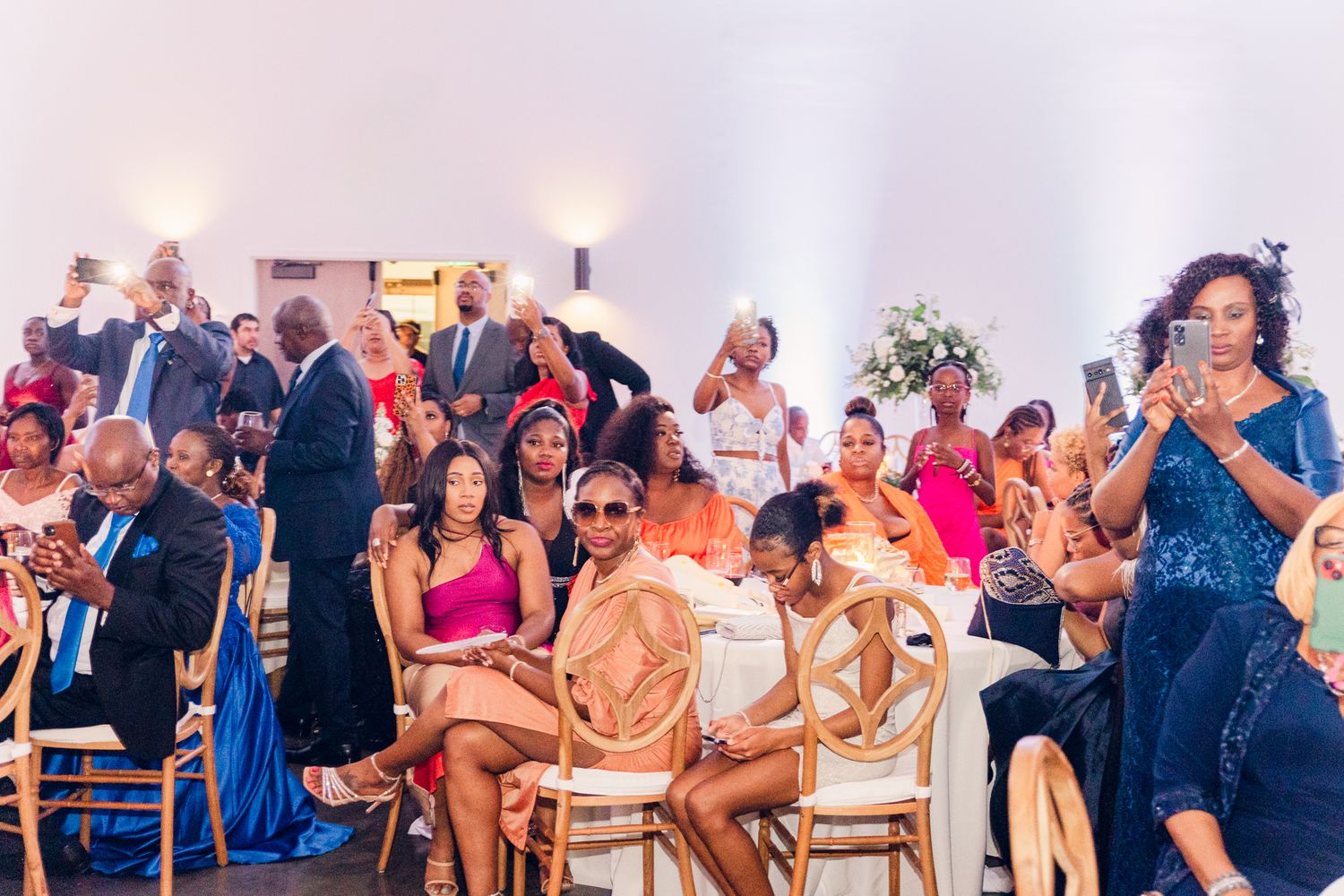 Wedding guests seated and standing in a bright reception hall with elegant decor.